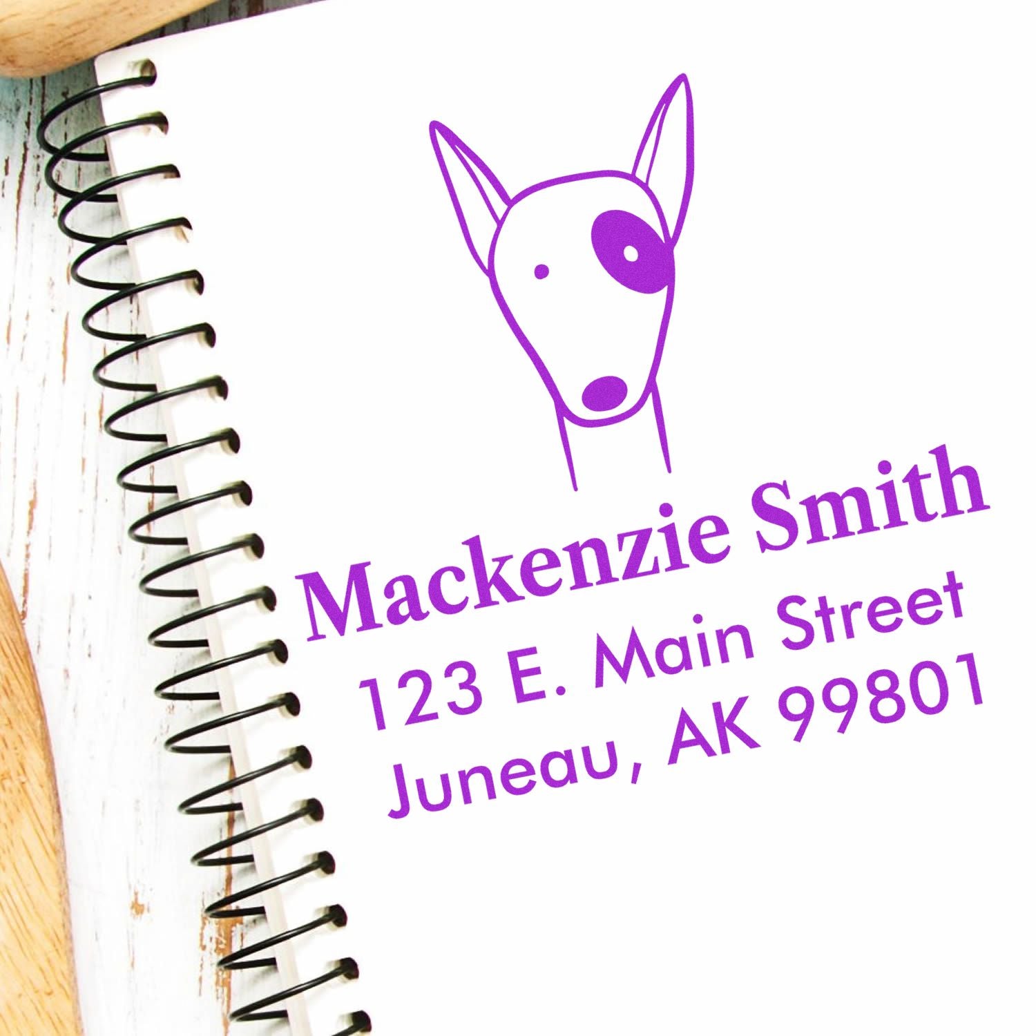 Wood handle delightful dog cartoon animal custom home stamper on a notebook. Personalized address stamp reads "Mackenzie Smith, 123 E. Main Street, Juneau, AK 99801" in purple ink.