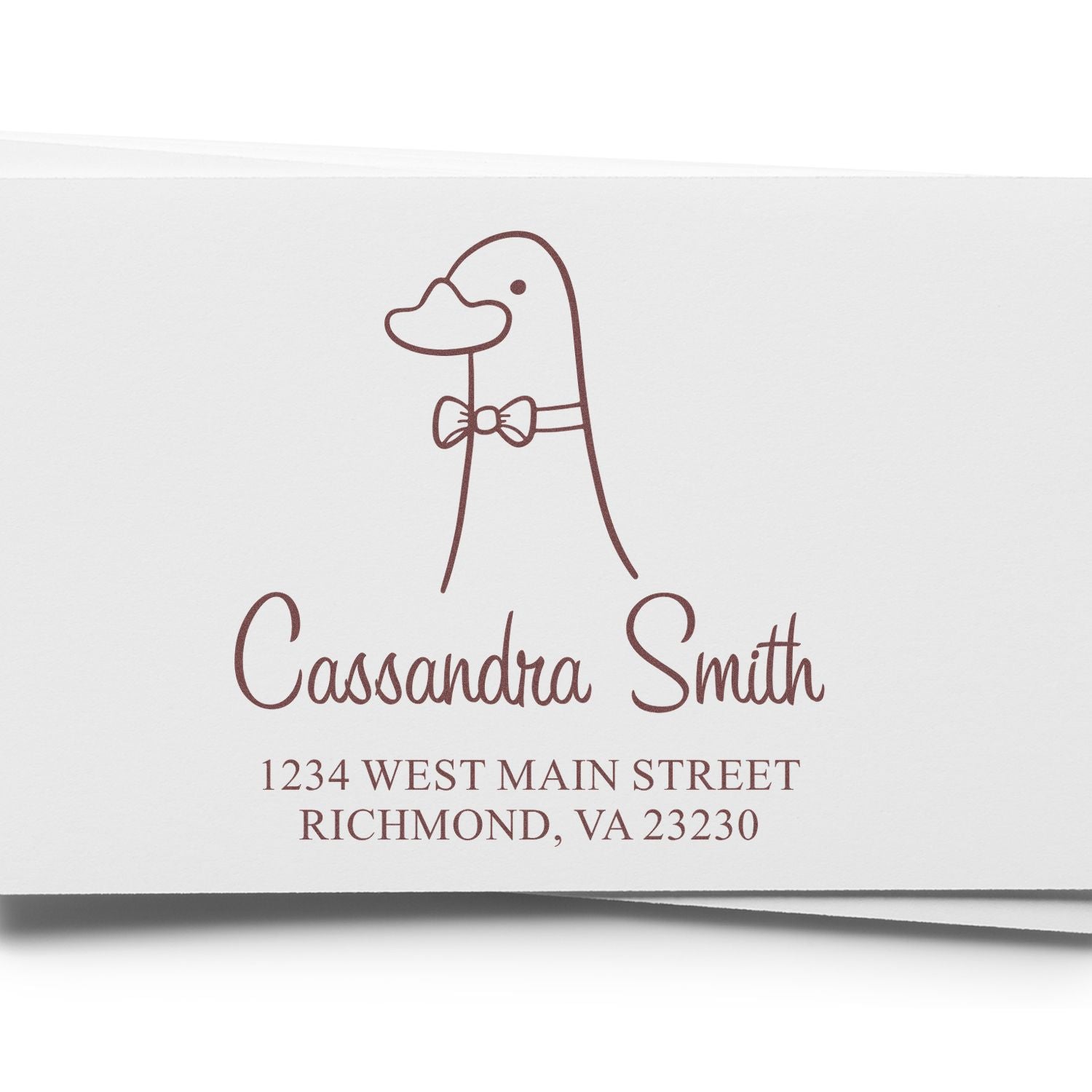 Wood handle dashing duck cartoon animal custom name and address stamper on white paper. The customizable mailing stamp features a duck with a bow tie, personalized with "Cassandra Smith, 1234 West Main Street, Richmond, VA 23230."