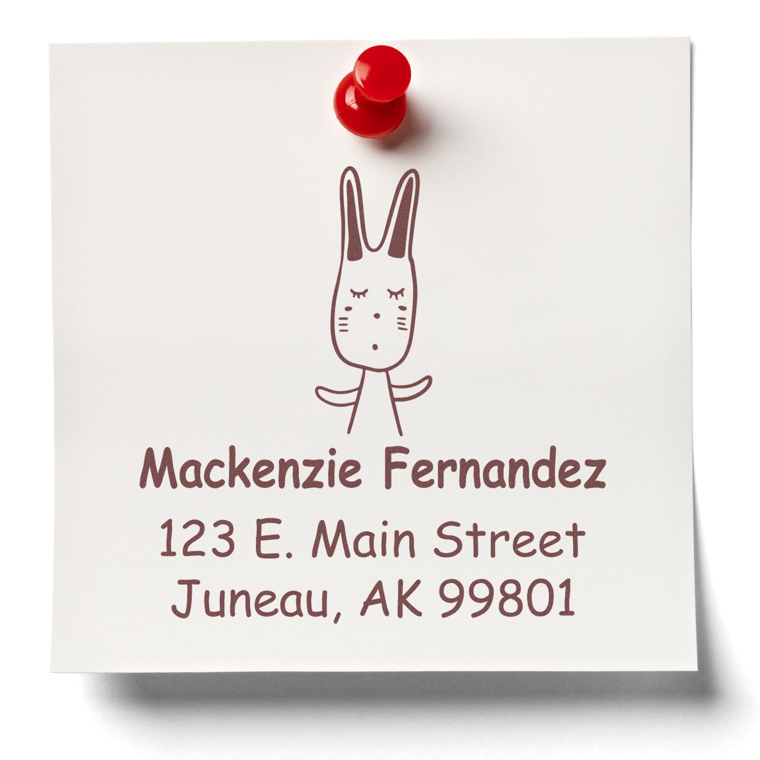 Wood Handle Hopping Bunny Cartoon Animal Custom Return Address Stamper on a white note with a red pushpin. The stamp features a cute bunny and is a personalizable home stamp with the address "Mackenzie Fernandez, 123 E. Main Street, Juneau, AK 99801."