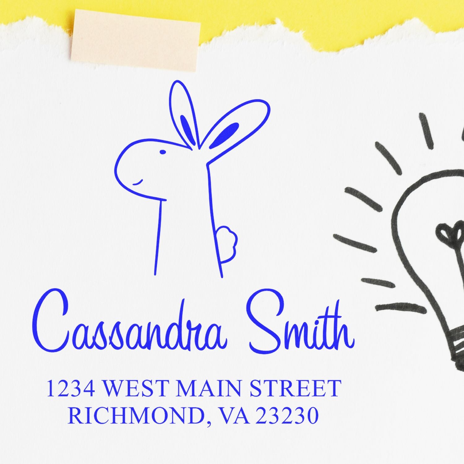 Wood Handle Bouncy Bunny Cartoon Animal Custom Return Address Stamp on white paper with a blue bunny illustration. Text reads "Cassandra Smith, 1234 West Main Street, Richmond, VA 23230." Customized Home Stamp design with a lightbulb sketch nearby.