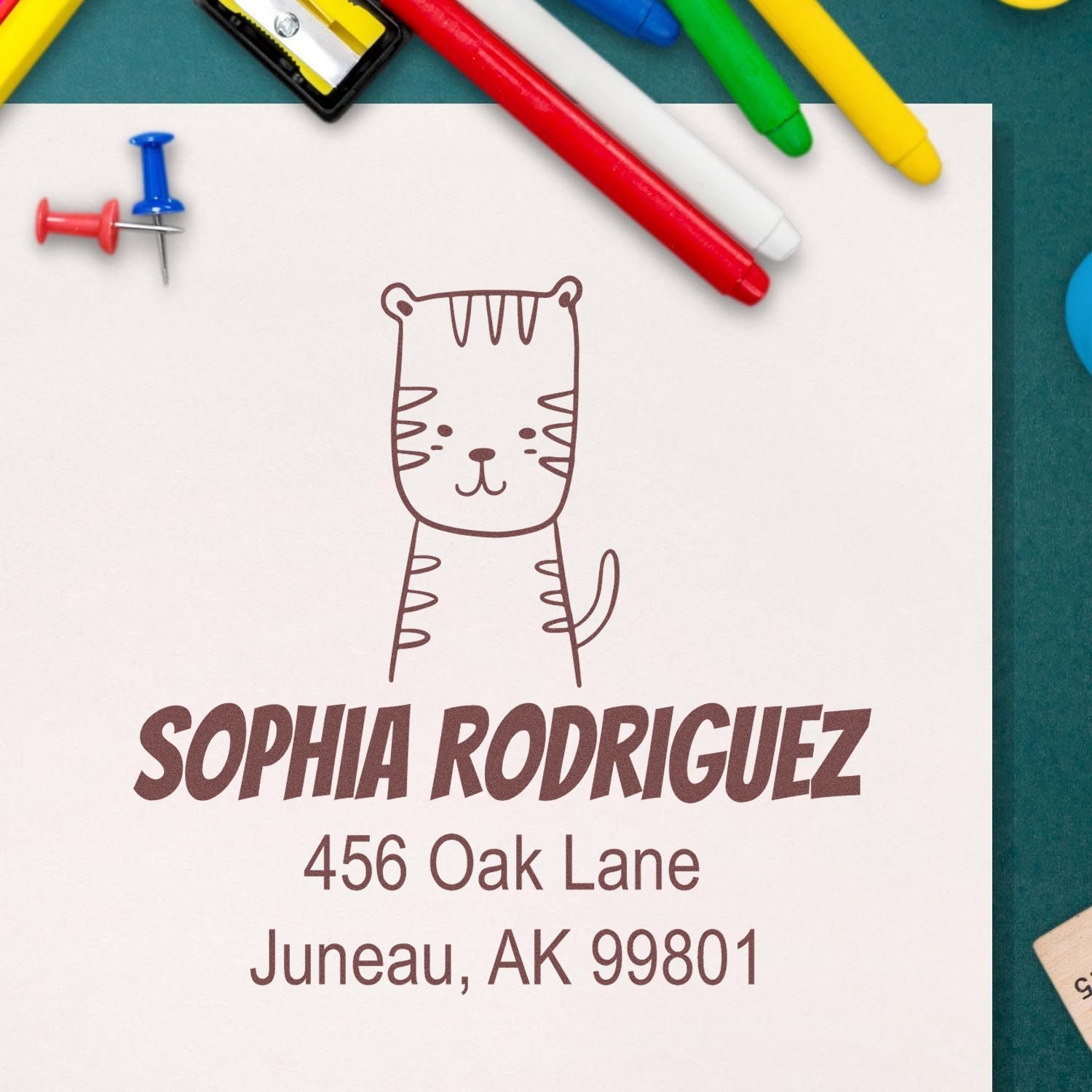 Wood Handle Terrific Tiger Cartoon Animal Custom Return Address Stamper on paper with "Sophia Rodriguez, 456 Oak Lane, Juneau, AK 99801." Surrounded by colorful pens and push pins. Customized Mailing Stamp for personalized correspondence.