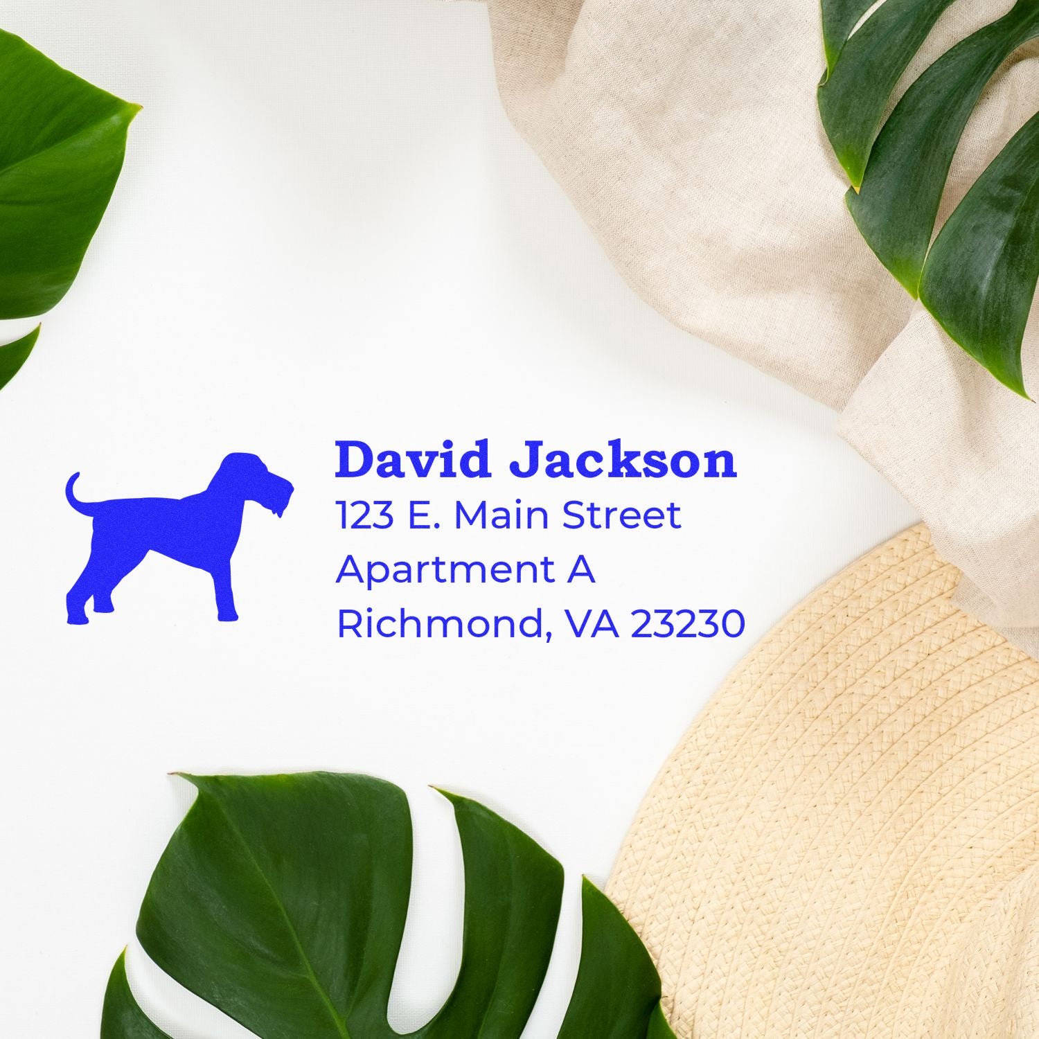 Slim Pre-Inked Airedale Terrier Address Stamp on white paper with green leaves and a beige hat. Blue ink displays a dog silhouette and sample address: David Jackson, 123 E. Main Street, Richmond, VA.