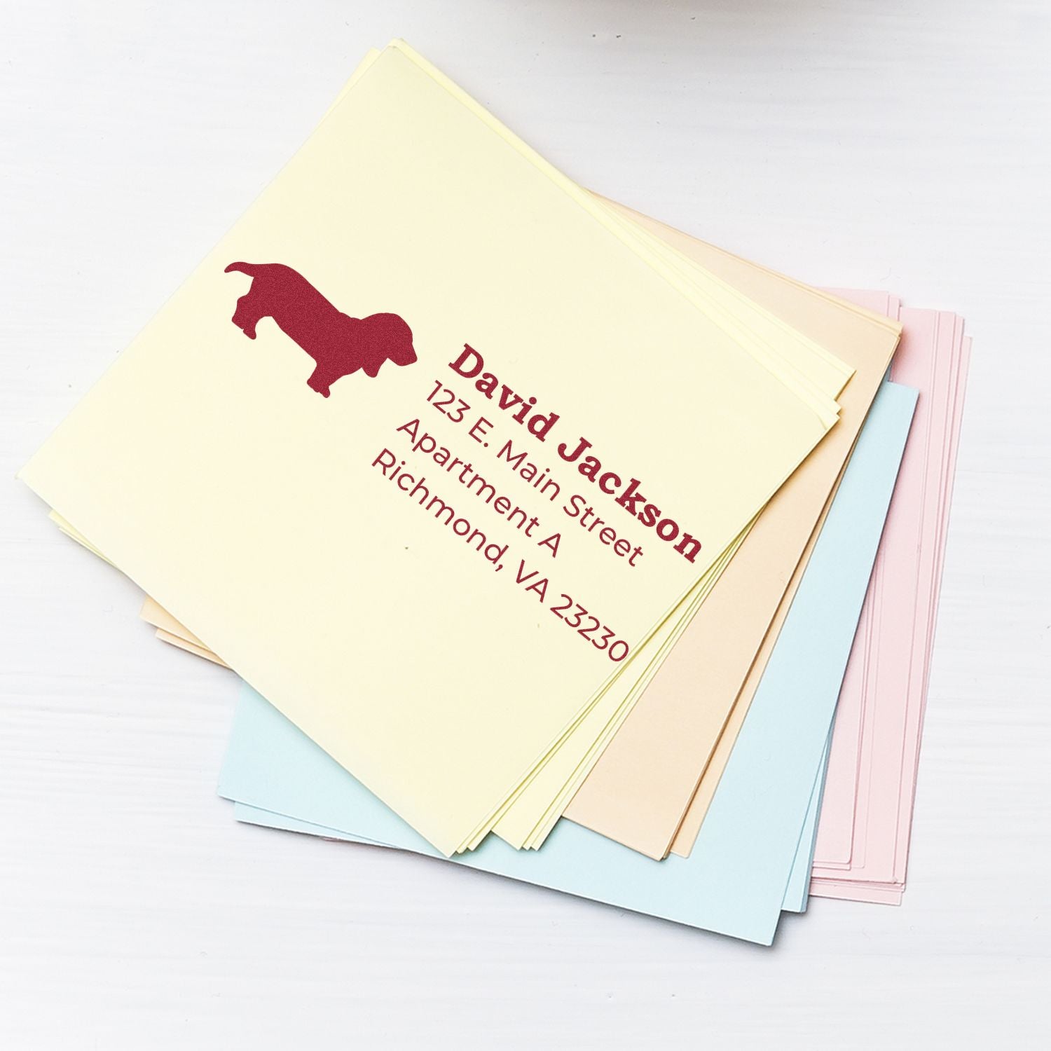 Stack of pastel envelopes featuring a Basset Hound Silhouette Address Rubber Stamp with red ink, displaying a sample address.