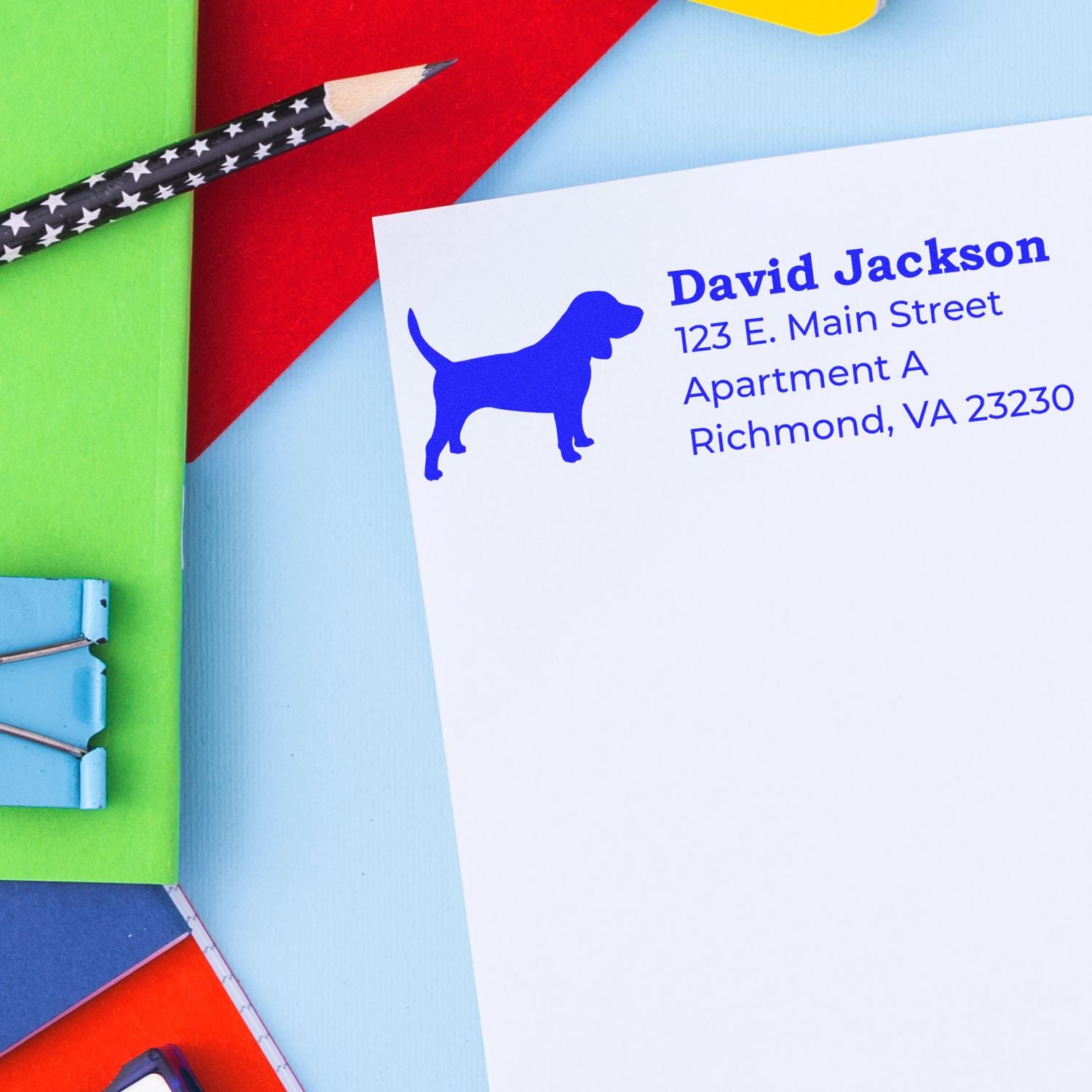 Beagle Silhouette Address Rubber Stamp on white paper with blue ink, featuring a beagle silhouette and address details. Background includes colorful stationery items like a pencil and paper clips.