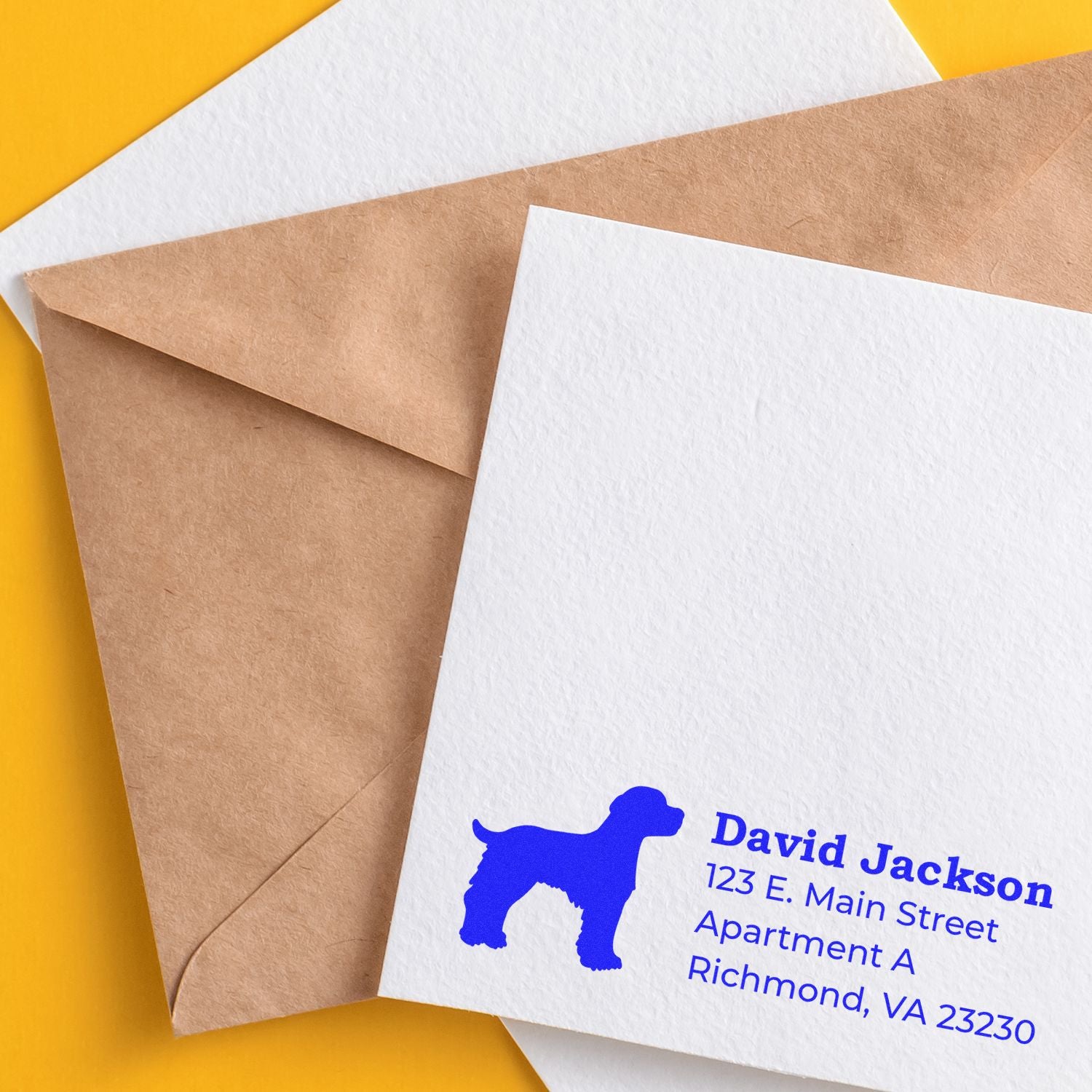 Self-Inking Brittany Spaniel Dog Address Stamp on a white envelope with a brown envelope beneath, featuring a blue dog silhouette and address text. Set against a vibrant yellow background.