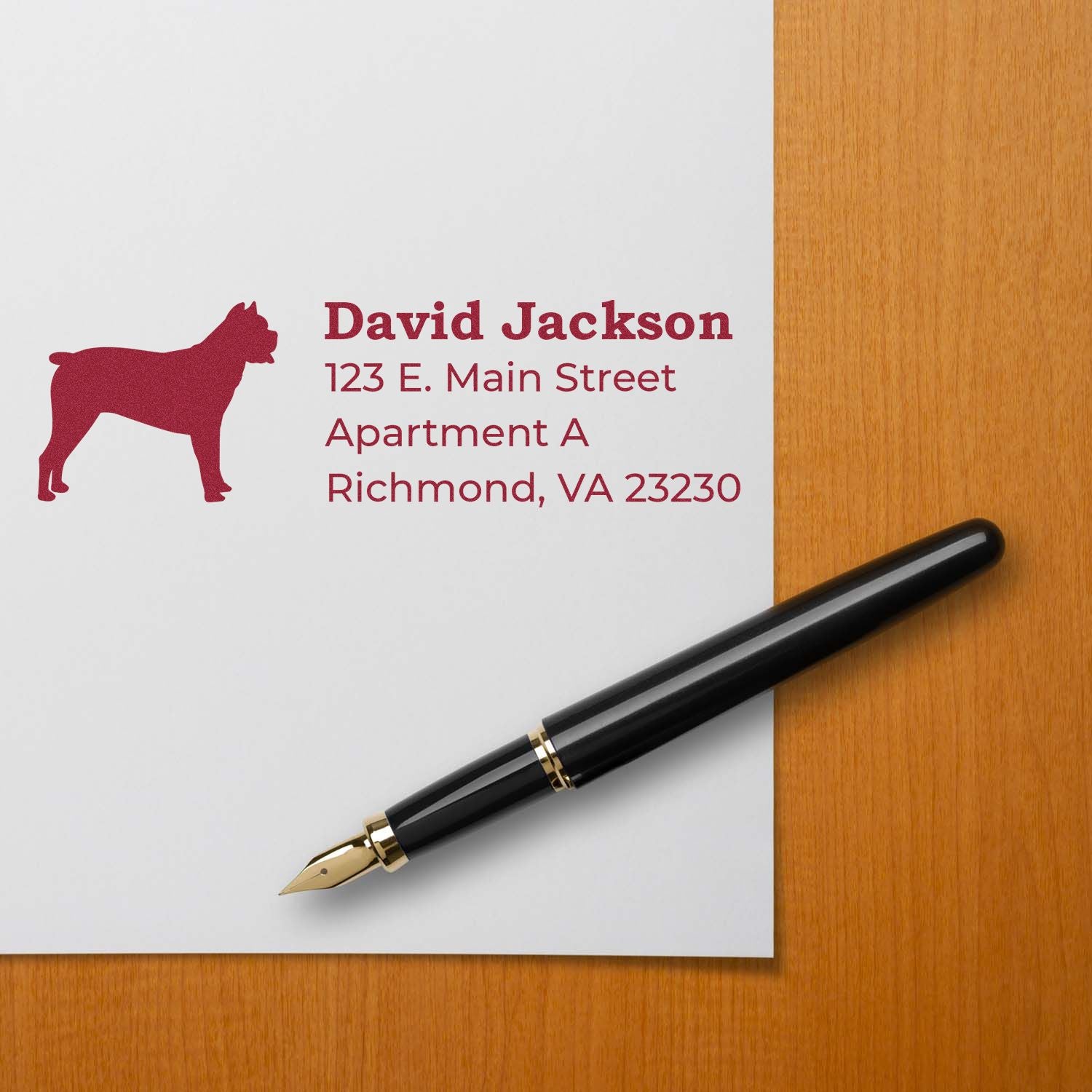 PSI Pre-Inked Personalized Cane Corso Address Stamp on paper with a black fountain pen, featuring a red Cane Corso silhouette and sample address text in red on a wooden surface.