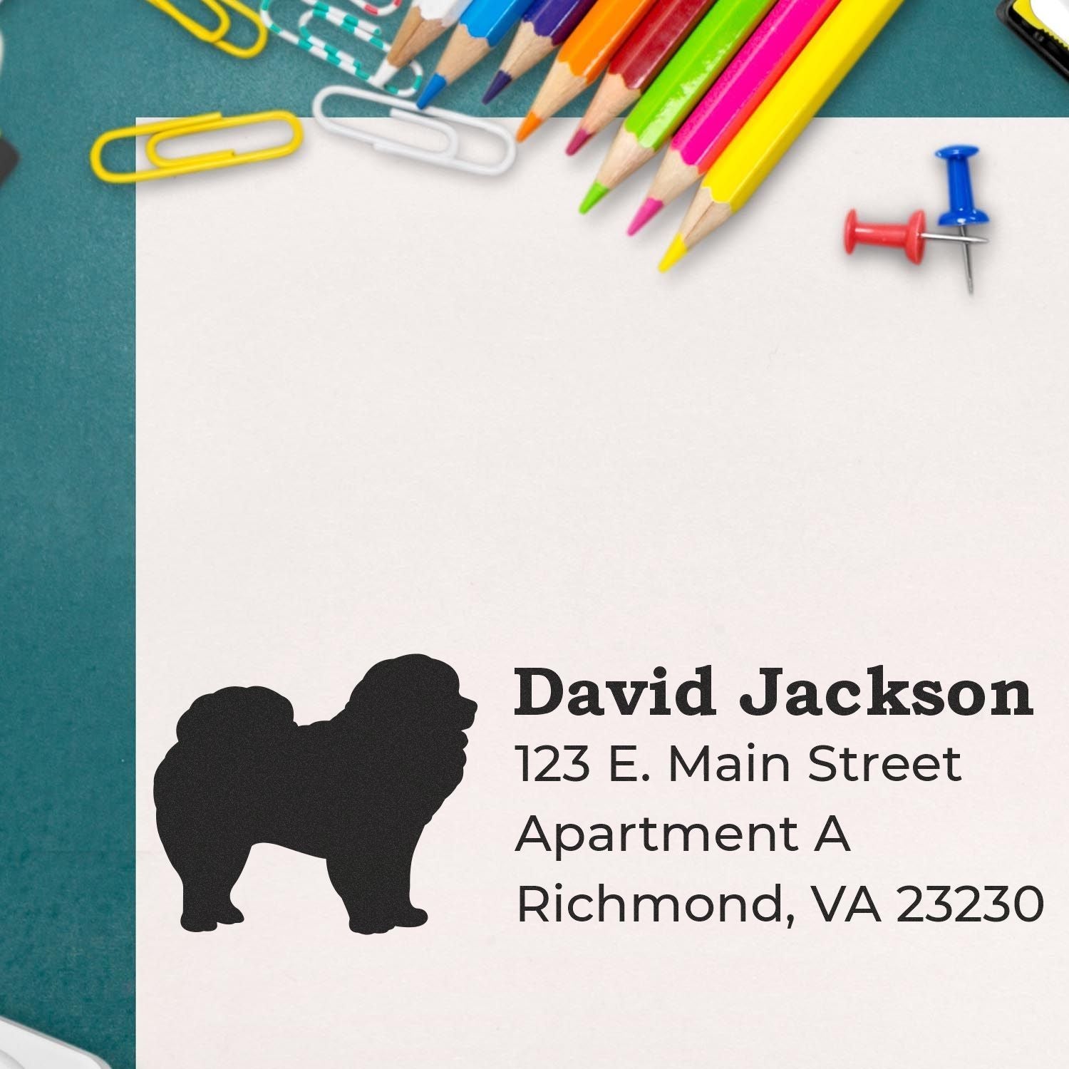 Self-Inking Chow Dog Address Stamp on paper with colorful pencils, paperclips, and pushpins. Features a silhouette of a Chow dog next to an address, showcasing its crisp, clear imprint.