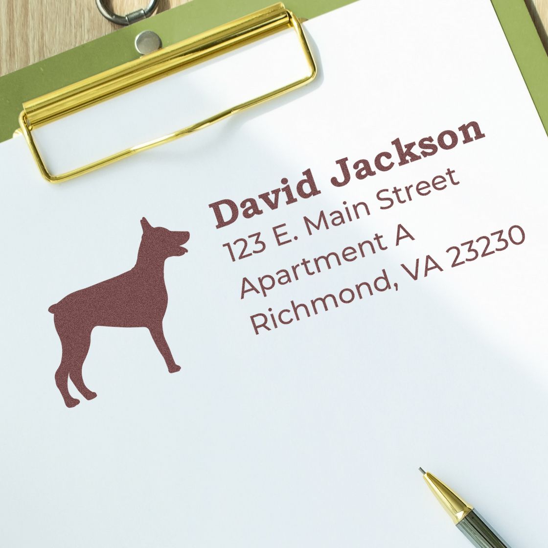 PSI Pre-Inked Personalized Doberman Address Stamp on paper with a Doberman silhouette and address details. Clipboard and pen nearby, showcasing the stamp's crisp, clear imprint.