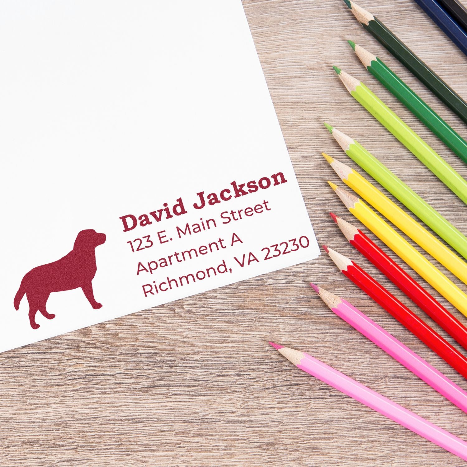 PSI Pre-Inked Personalized Labrador Address Stamp on paper with a Labrador silhouette, surrounded by colorful pencils on a wooden surface.