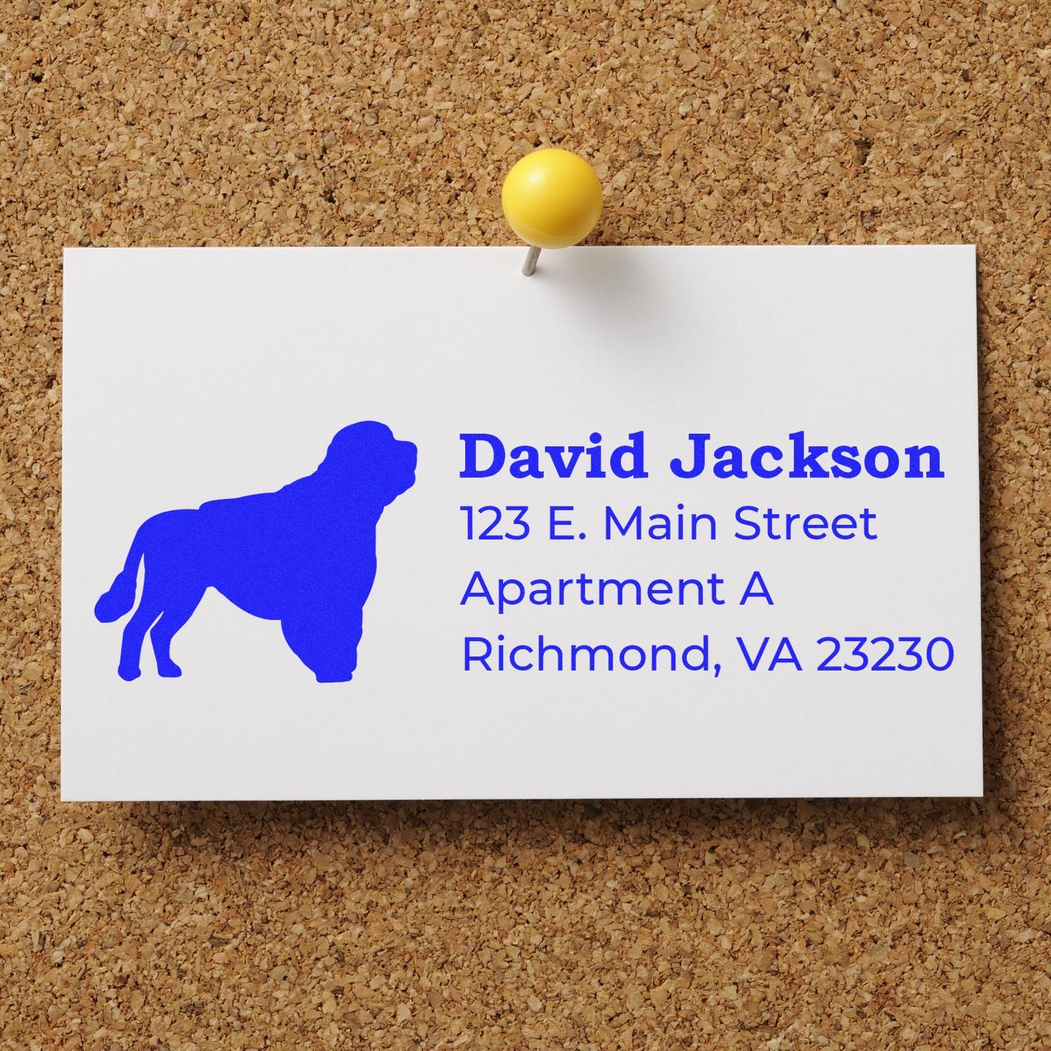 Self-Inking Portuguese Water Dog Address Stamp on a white card pinned to a corkboard, featuring a blue silhouette of the dog and sample address text in bold blue font.