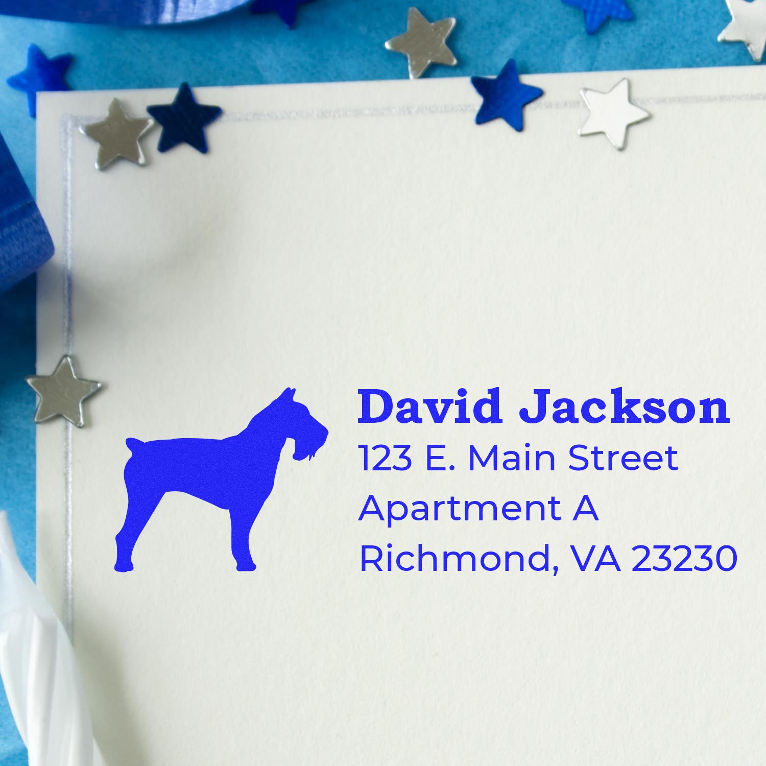 Self-Inking Schnauzer Dog Address Stamp on an envelope with a blue schnauzer silhouette and address. Surrounded by blue and silver star decorations on a light blue background.