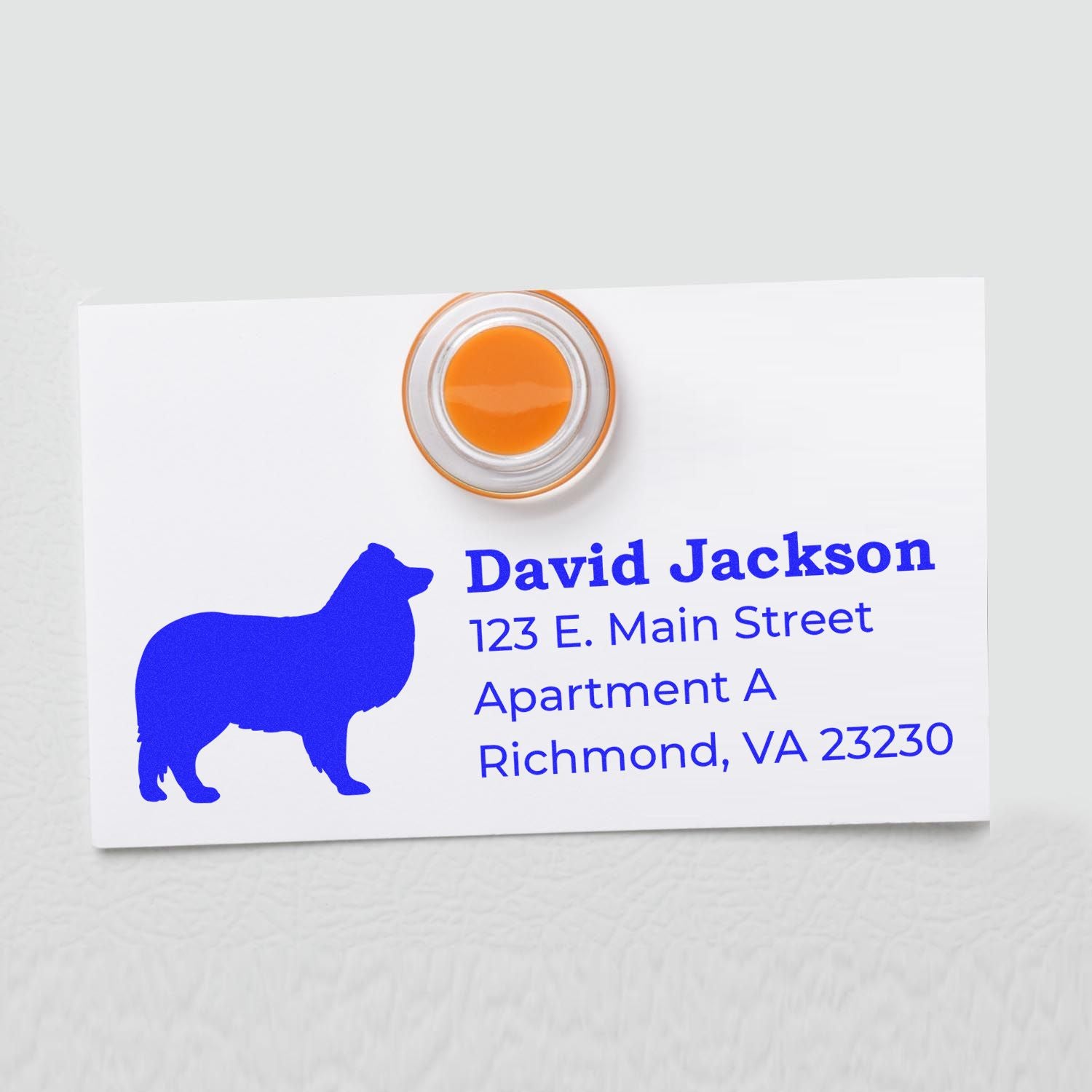 Slim Pre-Inked Shetland Sheepdog Address Stamp on a white card with blue text and a silhouette of a Shetland Sheepdog. The stamp is round with an orange center, showcasing a clean, professional imprint.