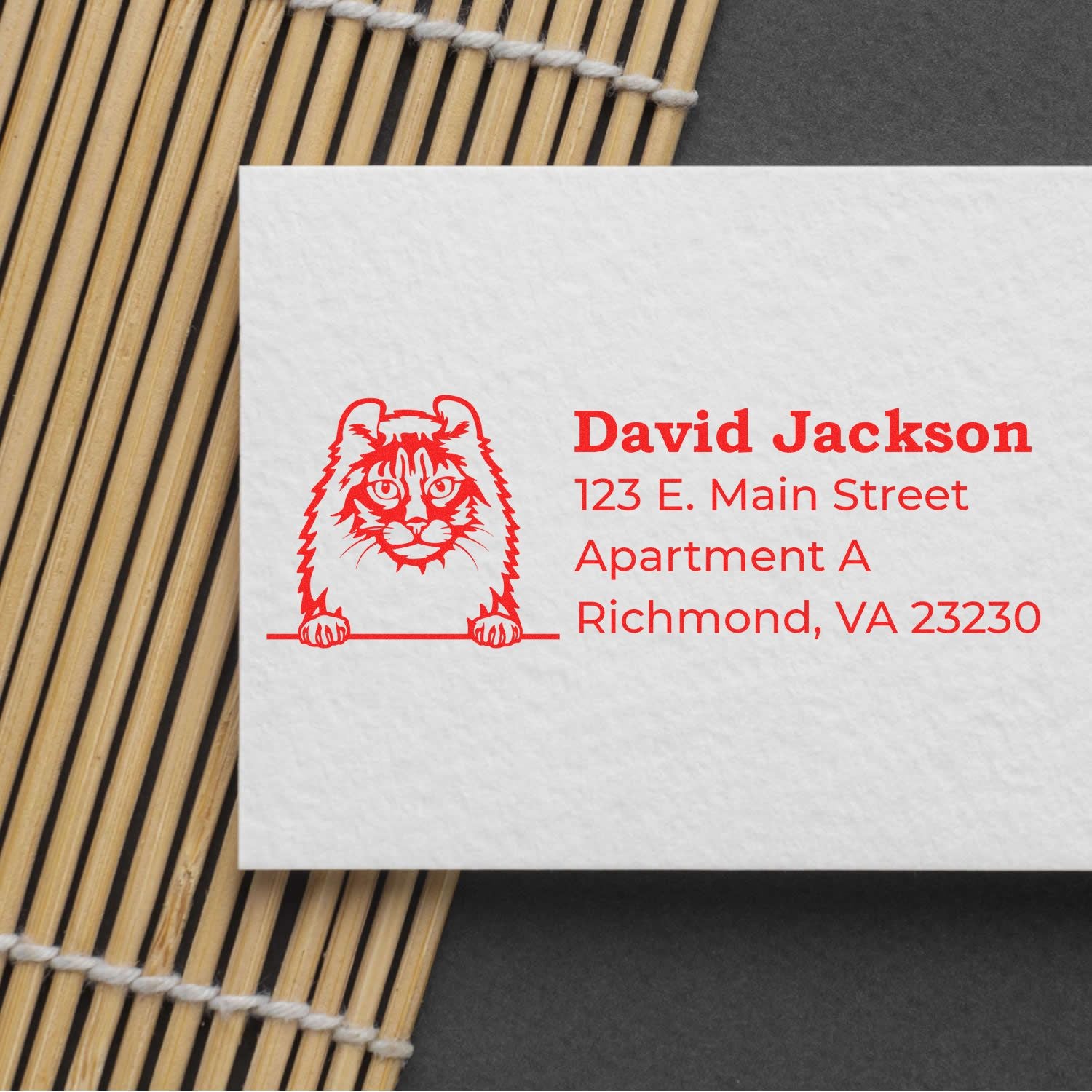 PSI Pre-Inked Peeking American Curl Cat Personalized Address Stamp on a card with red text and cat design, placed on a bamboo mat and dark background.