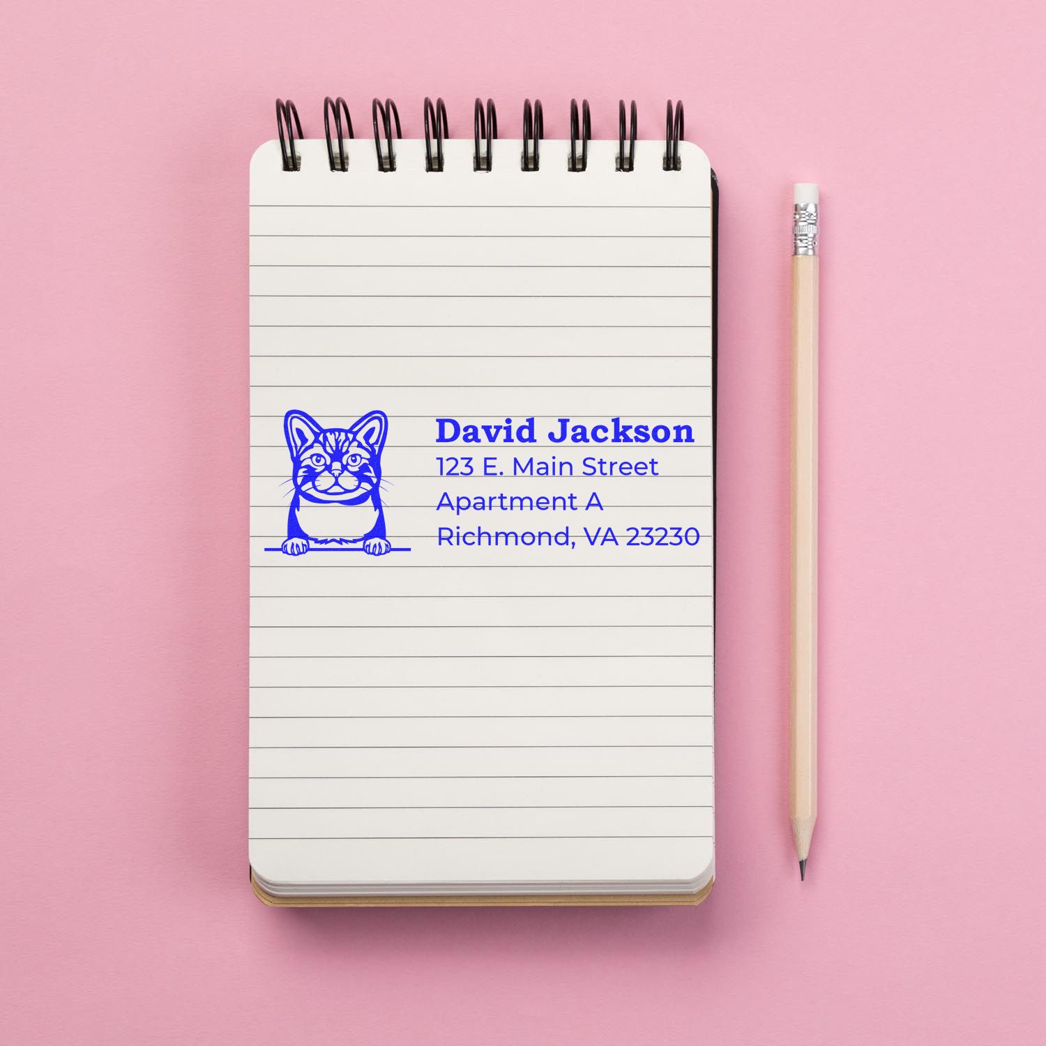 Self-Inking American Wirehair Custom Address Stamp on a notepad with a pencil on a pink background, featuring a cat design and sample address text in blue ink.