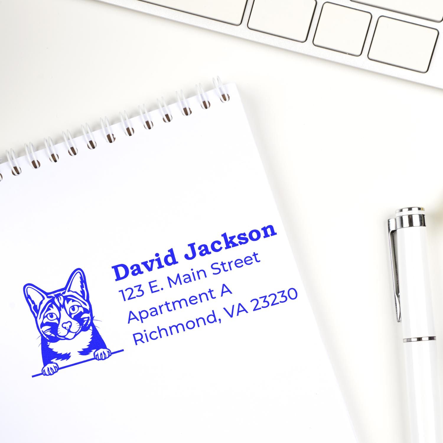 Wood Handle Arabian Mau Cat Address Stamp on notepad with blue ink, featuring a cat illustration and sample address. Pen and keyboard nearby, showcasing a stylish and practical desk accessory.