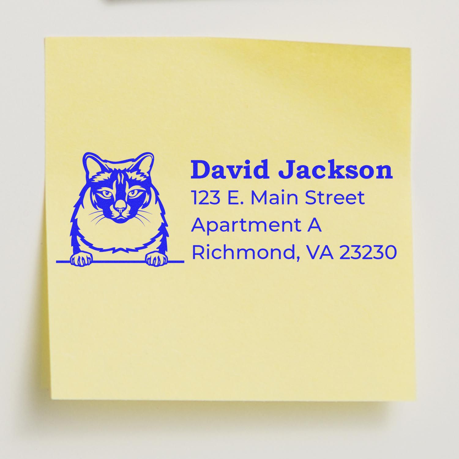 Yellow sticky note with blue ink impression from Wood Handle Balinese Cat Address Stamp, featuring a cat illustration and sample address: David Jackson, 123 E. Main Street, Richmond, VA 23230.