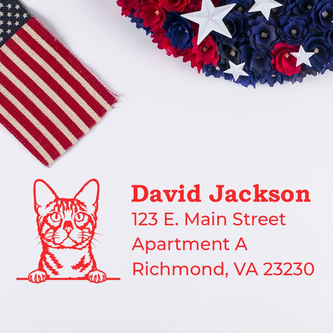 Wood Handle Bengal Cat Address Stamp on white paper with a red cat design, next to a decorative American flag and floral arrangement.