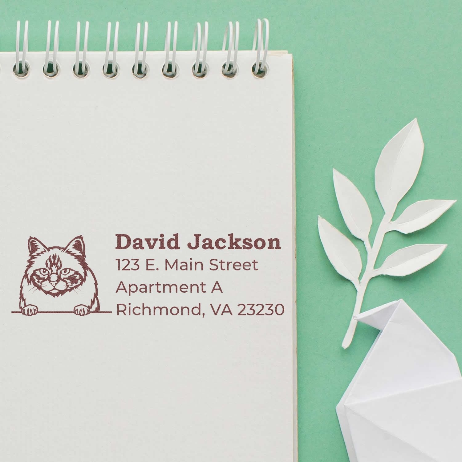 Wood Handle Birman Cat Address Stamp on a notepad with a stamped cat design and address. Features a green background, paper leaf, and origami bird for a stylish, personalized touch.