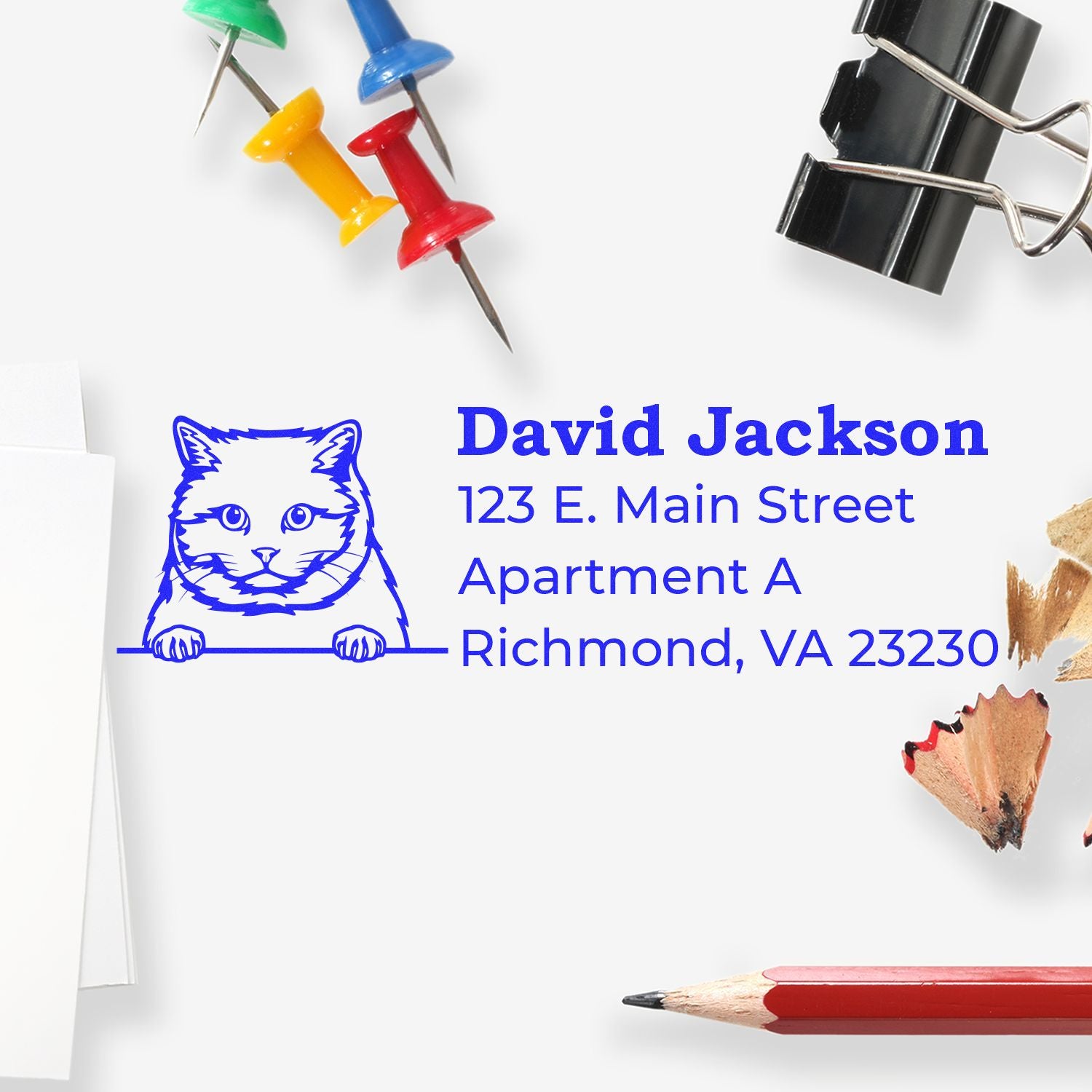 Self-Inking British Shorthair Custom Address Stamp on paper with a cat design, surrounded by colorful push pins, binder clip, pencil, and shavings.