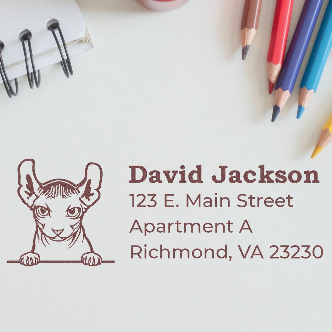 Wood Handle Dwelf Cat Address Stamp on paper with a cute cat illustration, surrounded by colored pencils and a notebook, showcasing a personalized address in elegant font.