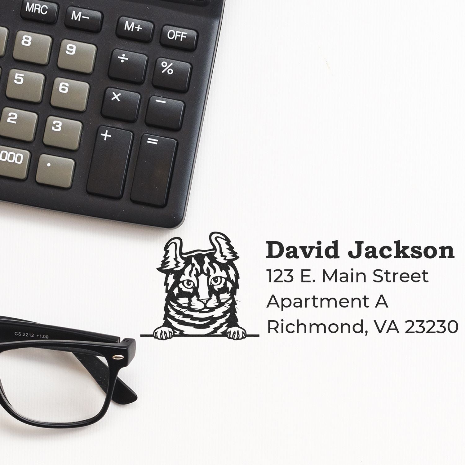 Self-Inking Highlander Custom Address Stamp on a desk with a calculator and glasses, featuring a playful cat design and sample address text.