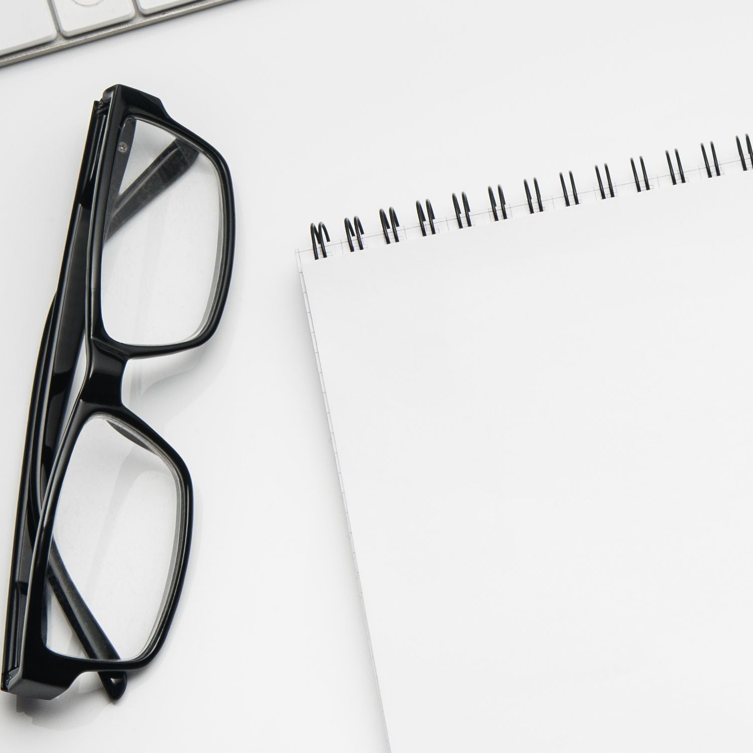 A Slim Pre-Inked Himalayan Peeking Cat Return Address Stamp on a white desk beside a spiral notebook and black glasses, showcasing its compact design and detailed cat illustration.