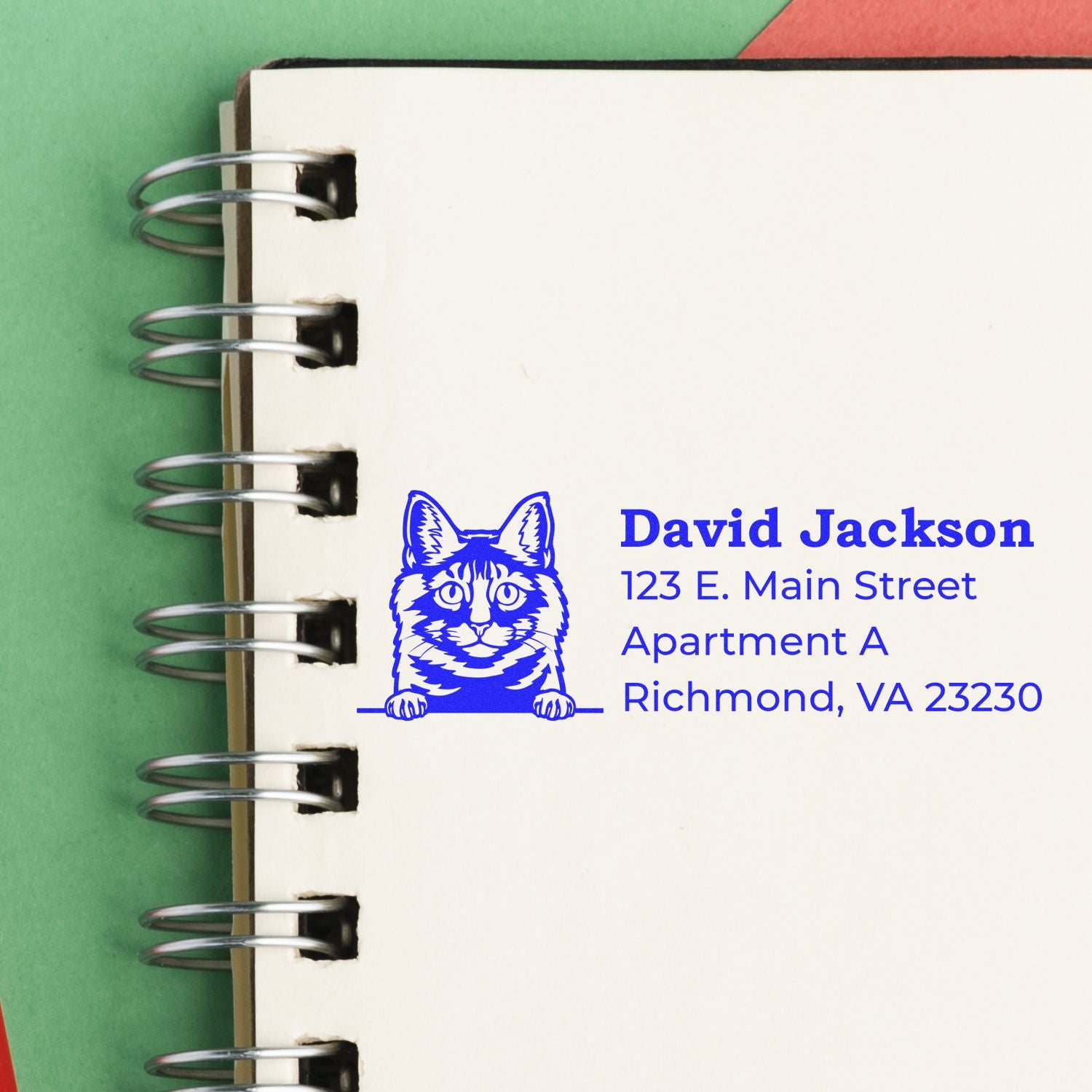 Slim Pre-Inked Kurilian Bobtail Peeking Cat Return Address Stamp on a notebook page, featuring a blue cat illustration with address details beside it. Perfect for personalizing mail with a playful touch.