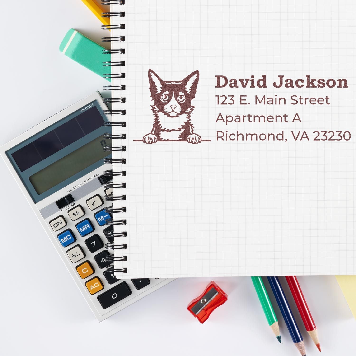 A notebook with a stamped LaPerm cat design and address, next to a calculator and colorful stationery. Showcasing the Wood Handle LaPerm Cat Address Stamp in use.