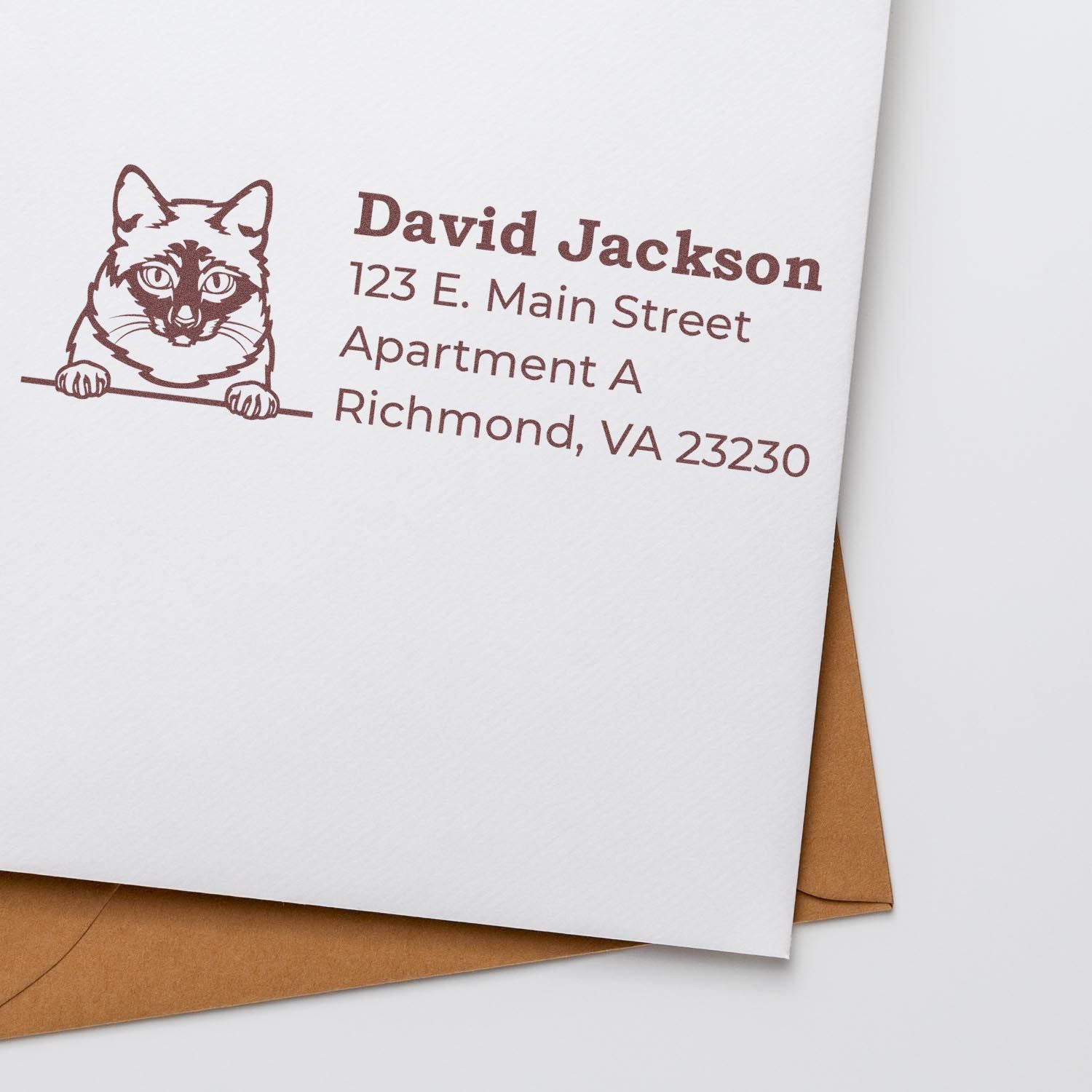 Wood Handle Mekong Bobtail Cat Address Stamp on white envelope with brown ink, featuring a cat illustration and sample address text. Brown envelope partially visible underneath.