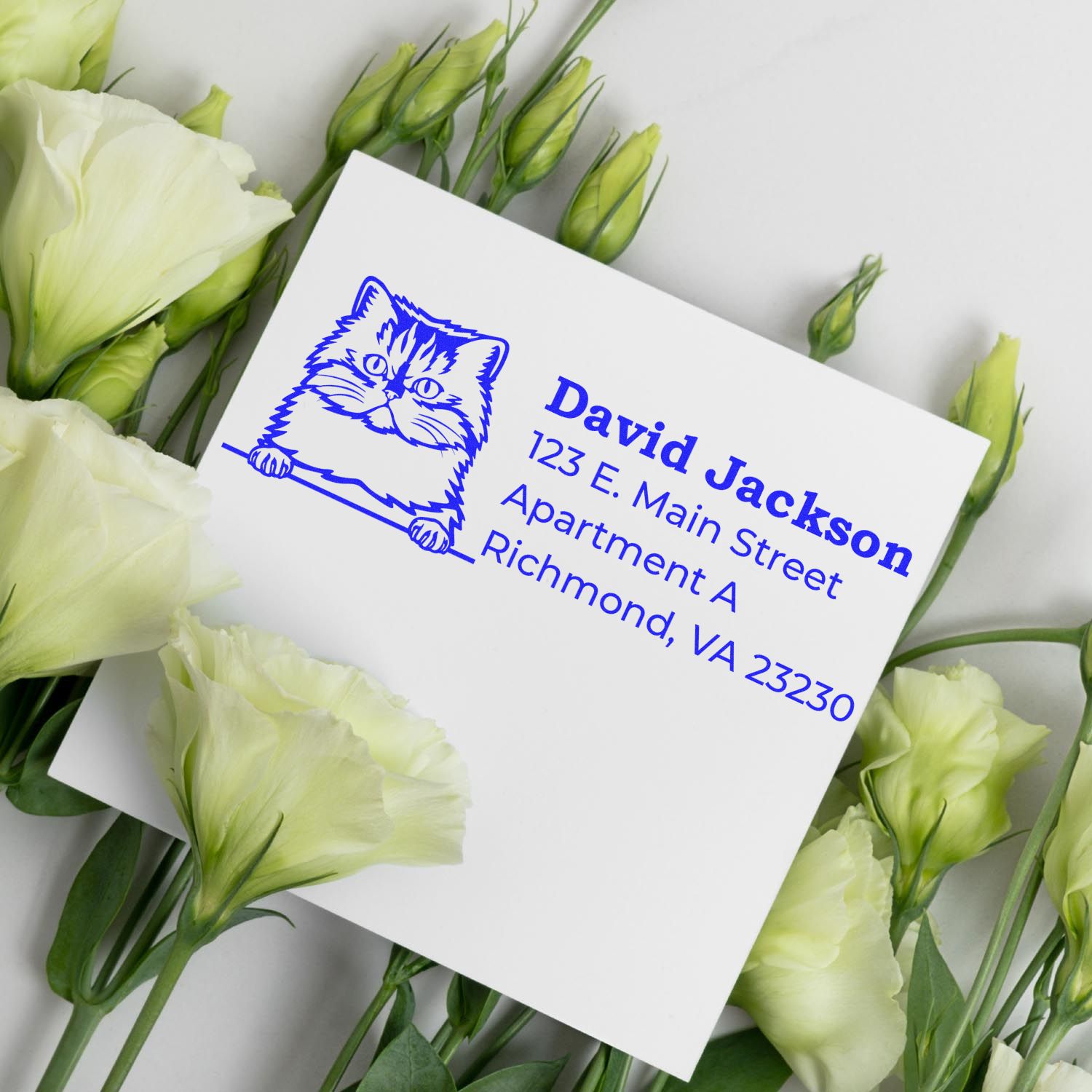 Self-Inking Persian Custom Address Stamp on white card with blue ink, featuring a Persian cat design. Surrounded by white flowers, showcasing elegant and personalized address labeling.