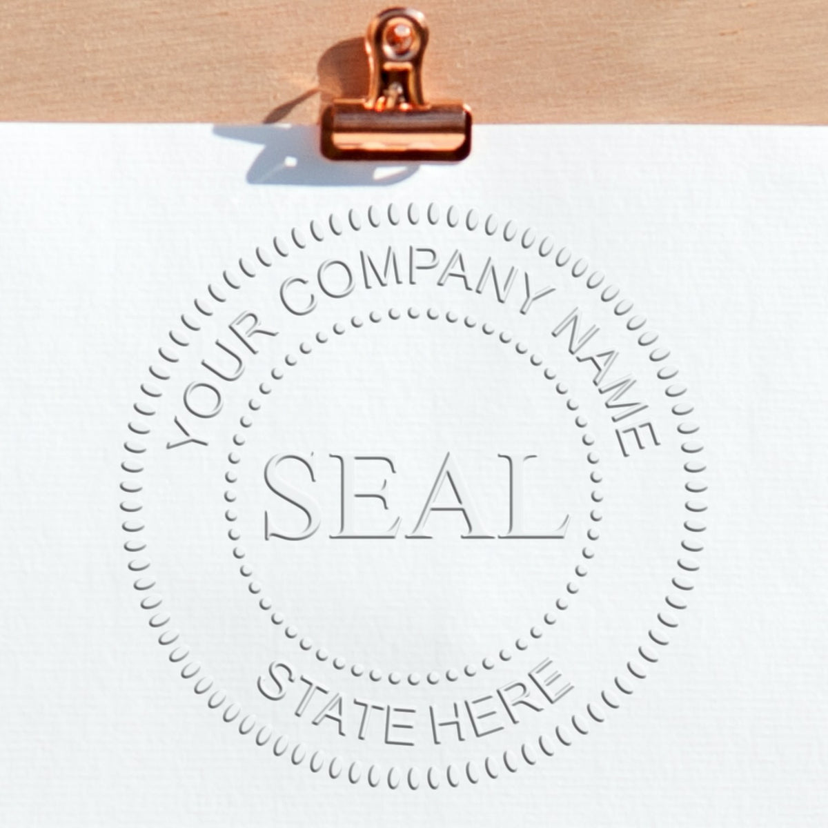 Copper clip holding white sheet with embossed company seal stamp, circular dotted border, and placeholder text.