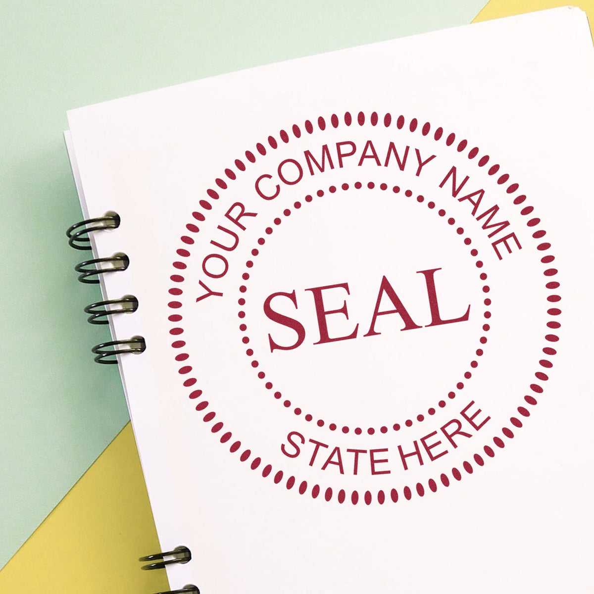 Custom maroon company seal stamp on white notebook page, with dotted circular border, spiral binding, and pastel green-yellow background.