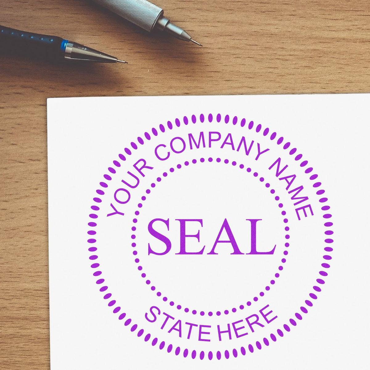 Purple custom company seal stamp on white paper with dotted border, on a wooden desk beside two pens.