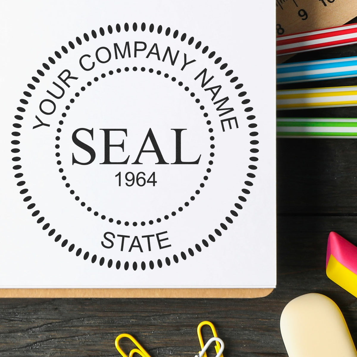 Black custom company seal stamp design on white paper, with dotted circle and colorful ink pads beside it.