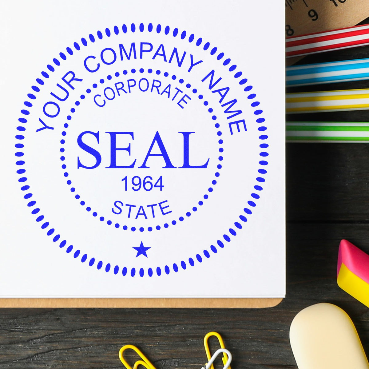 Blue custom company seal stamp on white paper with dotted border, star, and 1964; colorful stamp pads beside it.