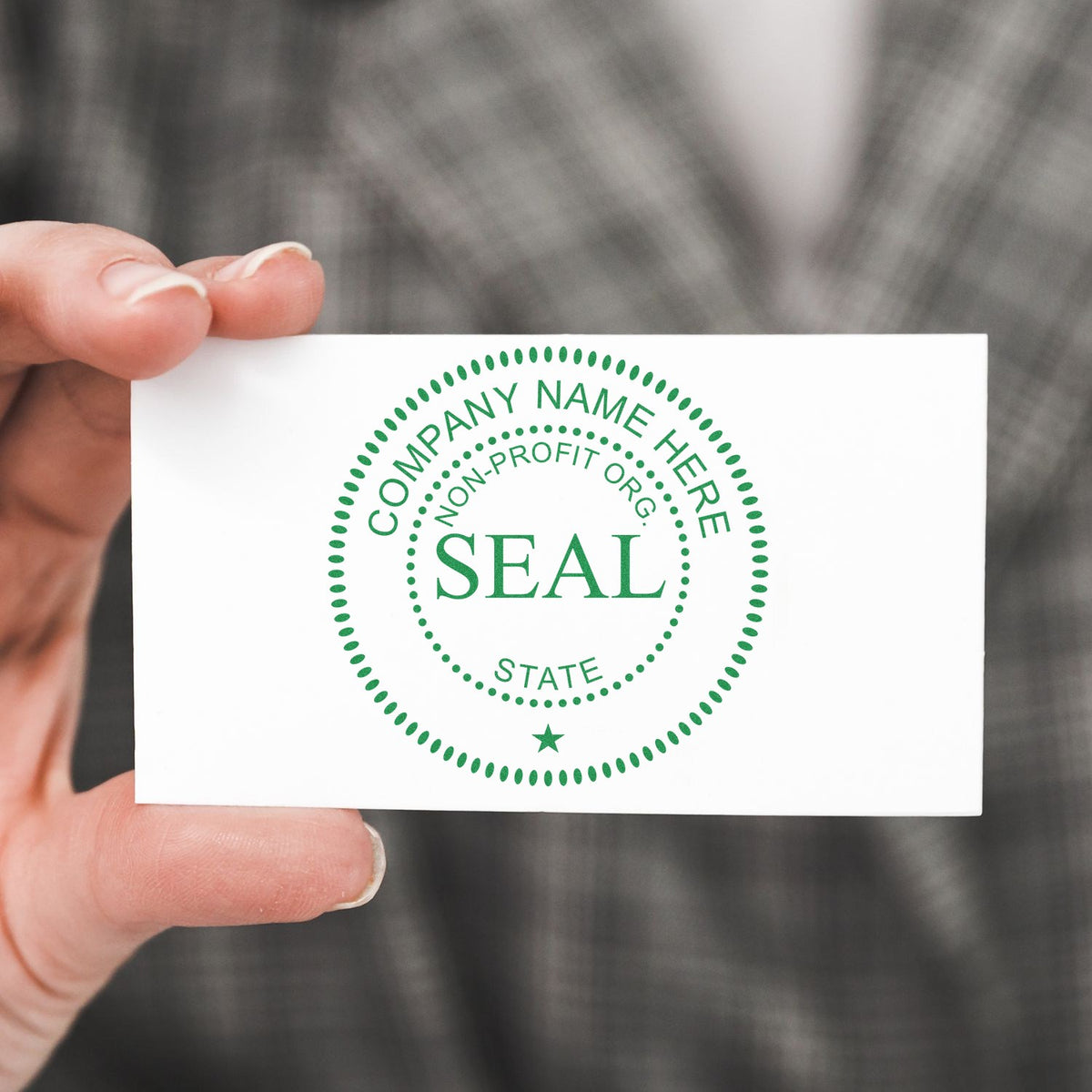 Hand holding white card featuring a green circular company seal stamp with dotted border and SEAL text.