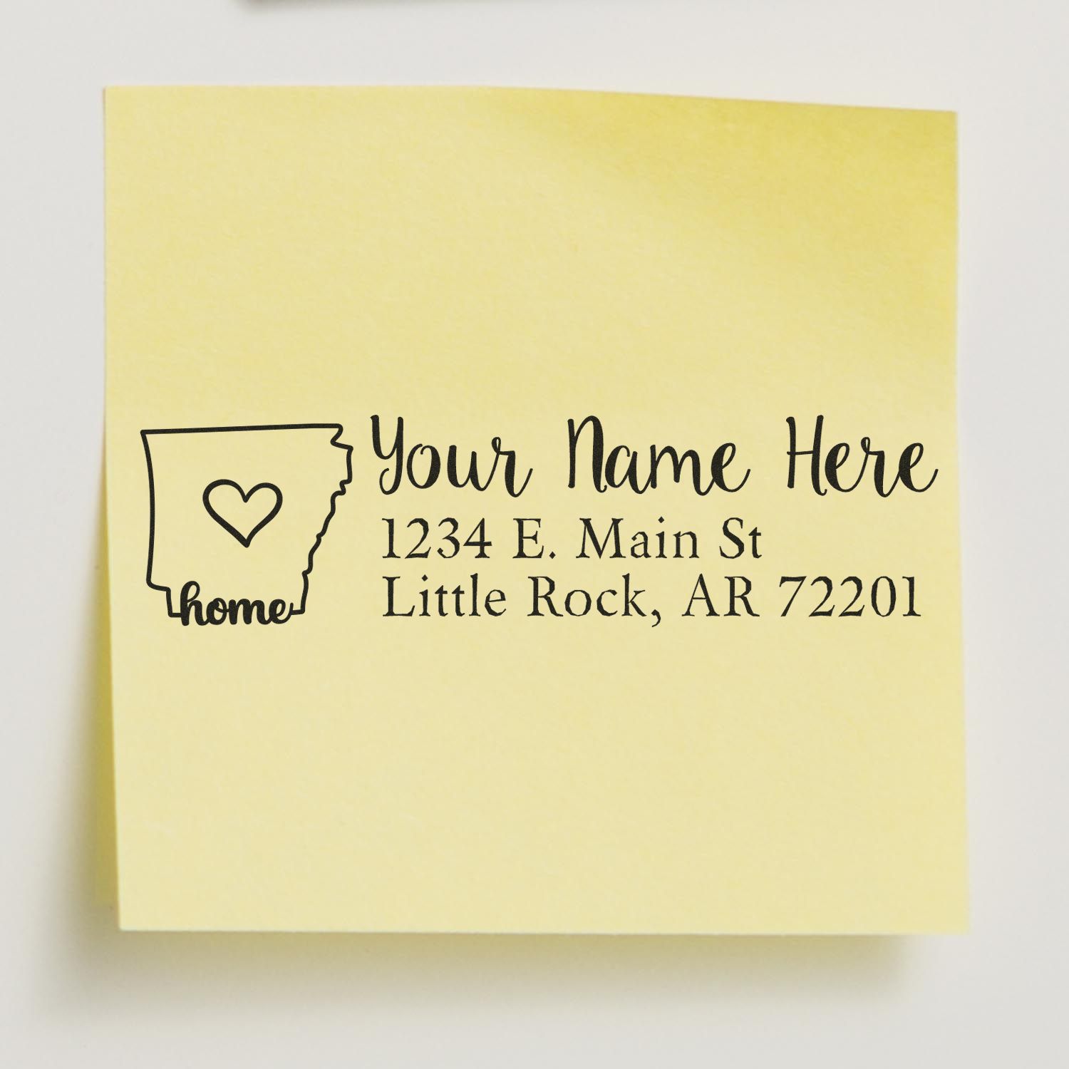 Yellow sticky note with the Arkansas Self-Inking State Love Address Stamp design, featuring a heart inside the state outline and sample address text: Your Name Here, 1234 E. Main St, Little Rock, AR 72201.