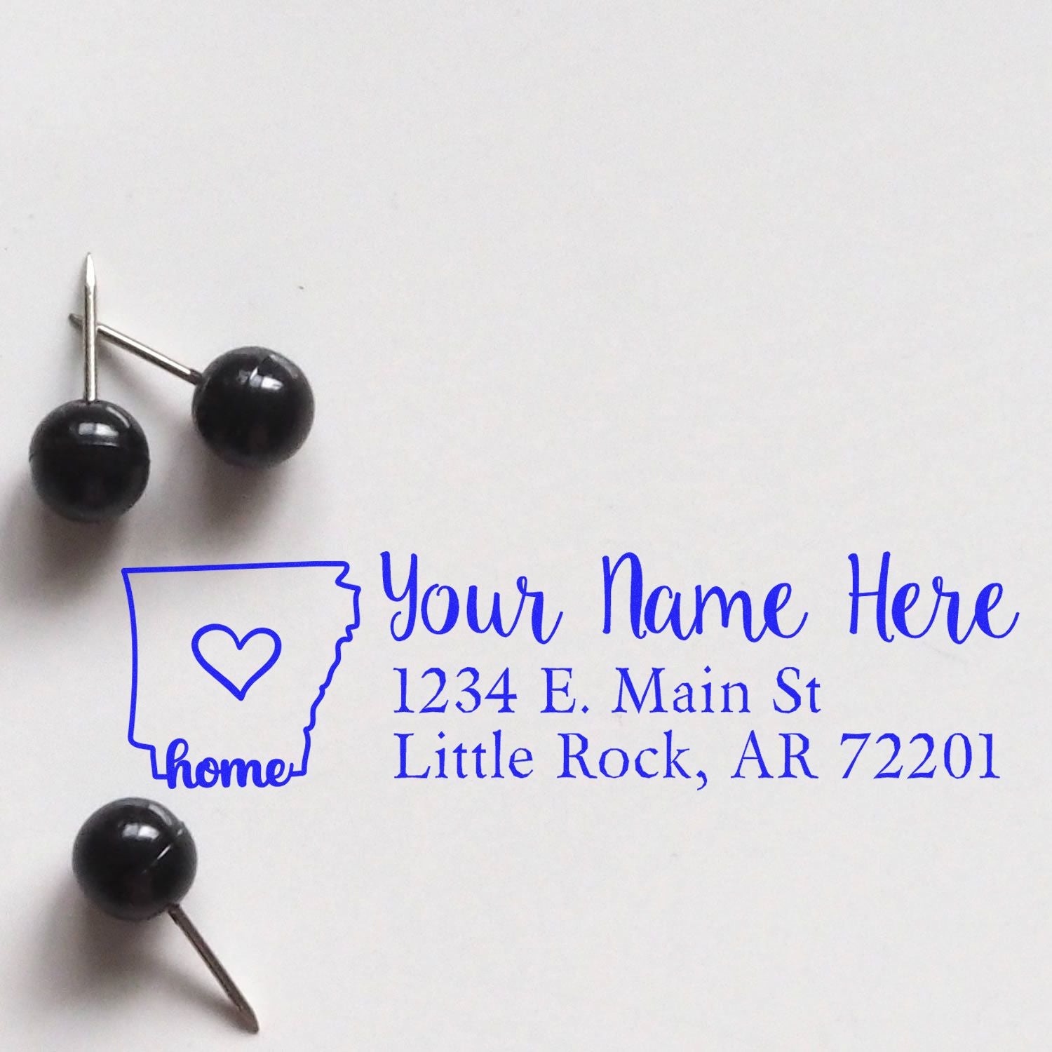 Wood Handle Arkansas Custom Address Rubber Stamp on white paper, featuring a heart inside the state outline and sample address text in blue. Two black push pins are placed nearby.