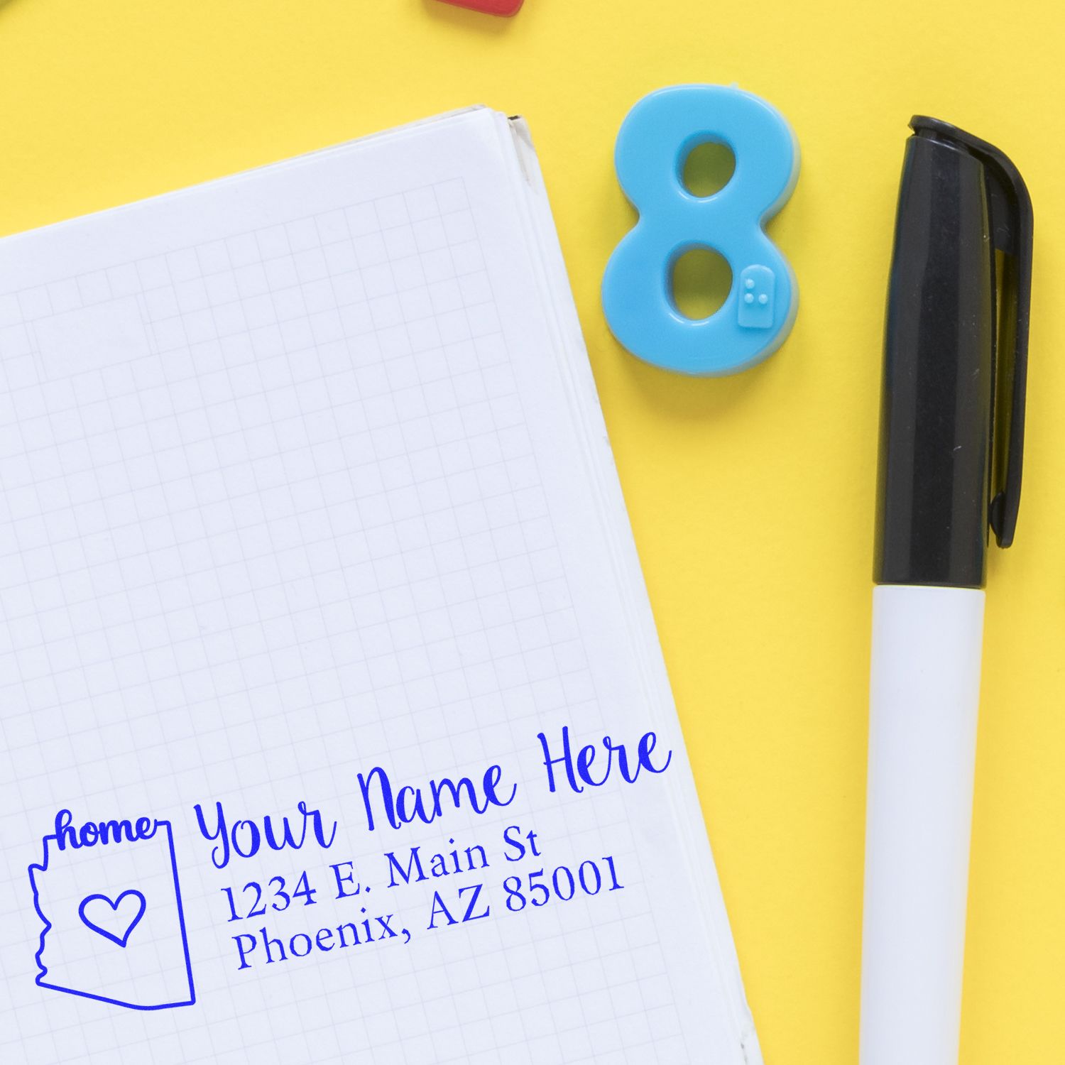 Arizona Self-Inking State Love Address Stamp on notepad with blue ink, showing a heart in Arizona outline, next to a pen and number 8 on a yellow background.