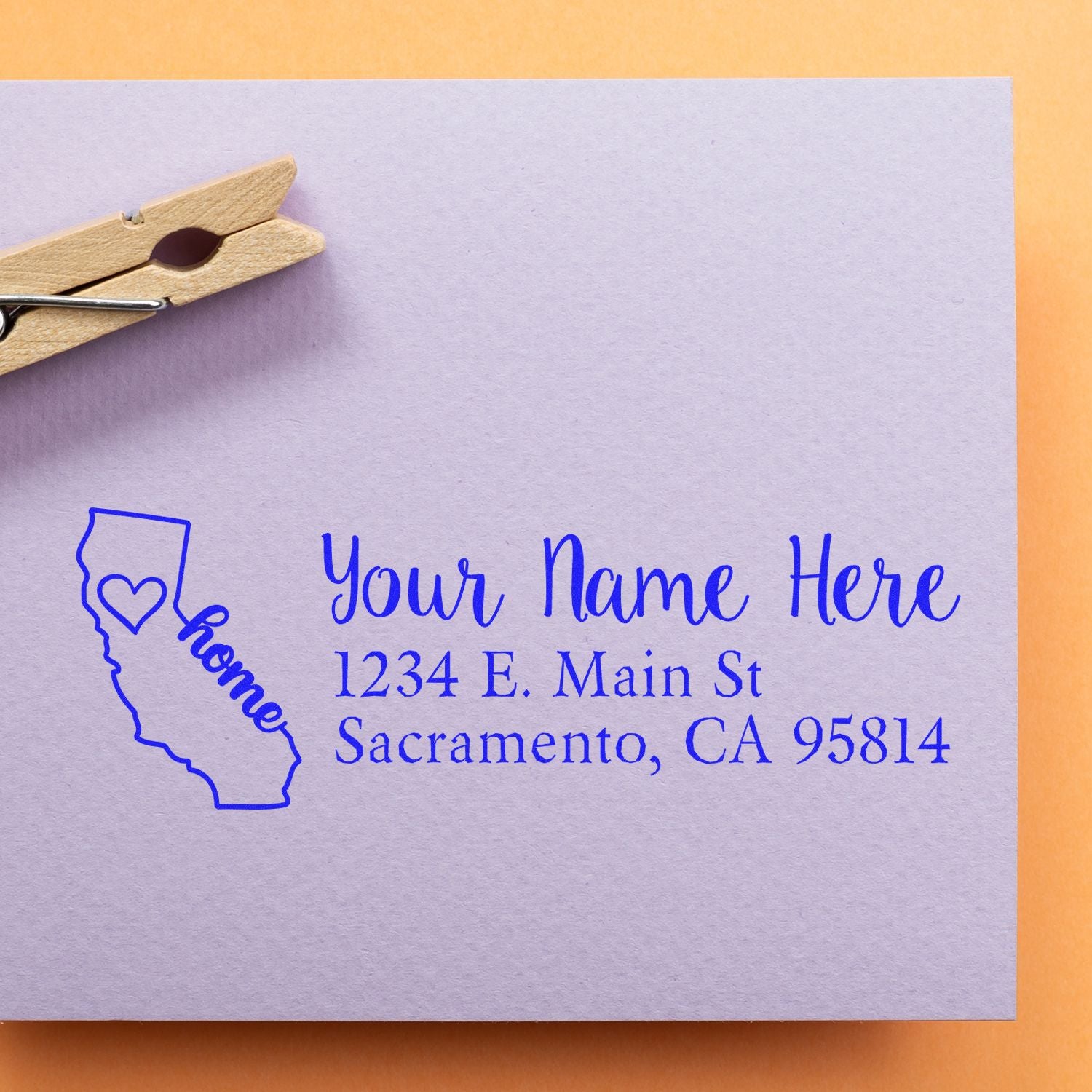 California Self-Inking State Love Address Stamp on a lavender envelope with a clothespin, featuring a heart and home text inside the state outline, personalized with name and address.