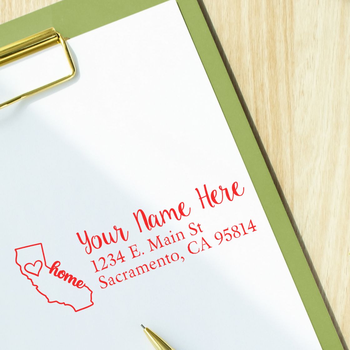 Wood Handle California Custom Address Rubber Stamp on paper with red ink, featuring a heart and state outline design, placed on a clipboard with a pen nearby.