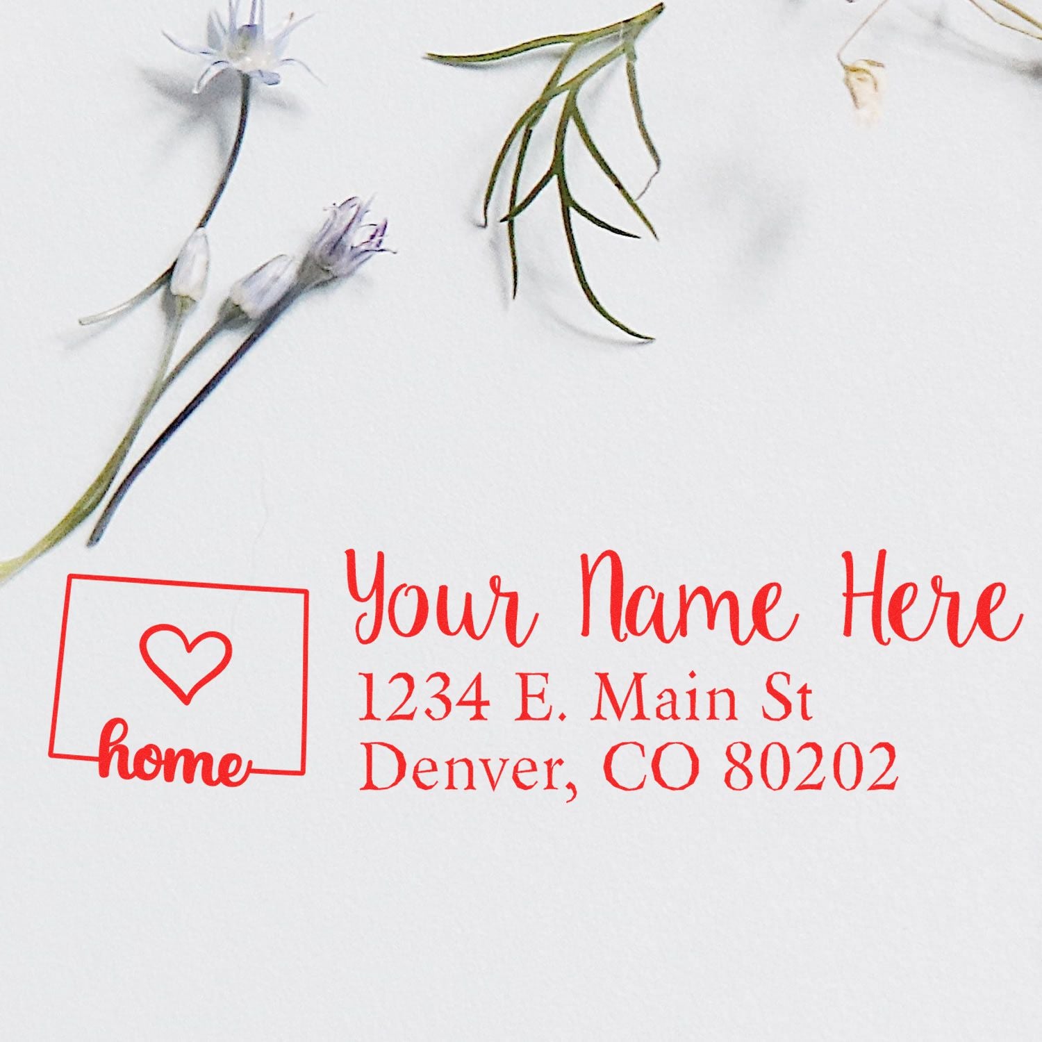 Wood Handle Colorado Custom Address Rubber Stamp in use, displaying a red address with a heart and home icon on white paper, surrounded by delicate flowers.