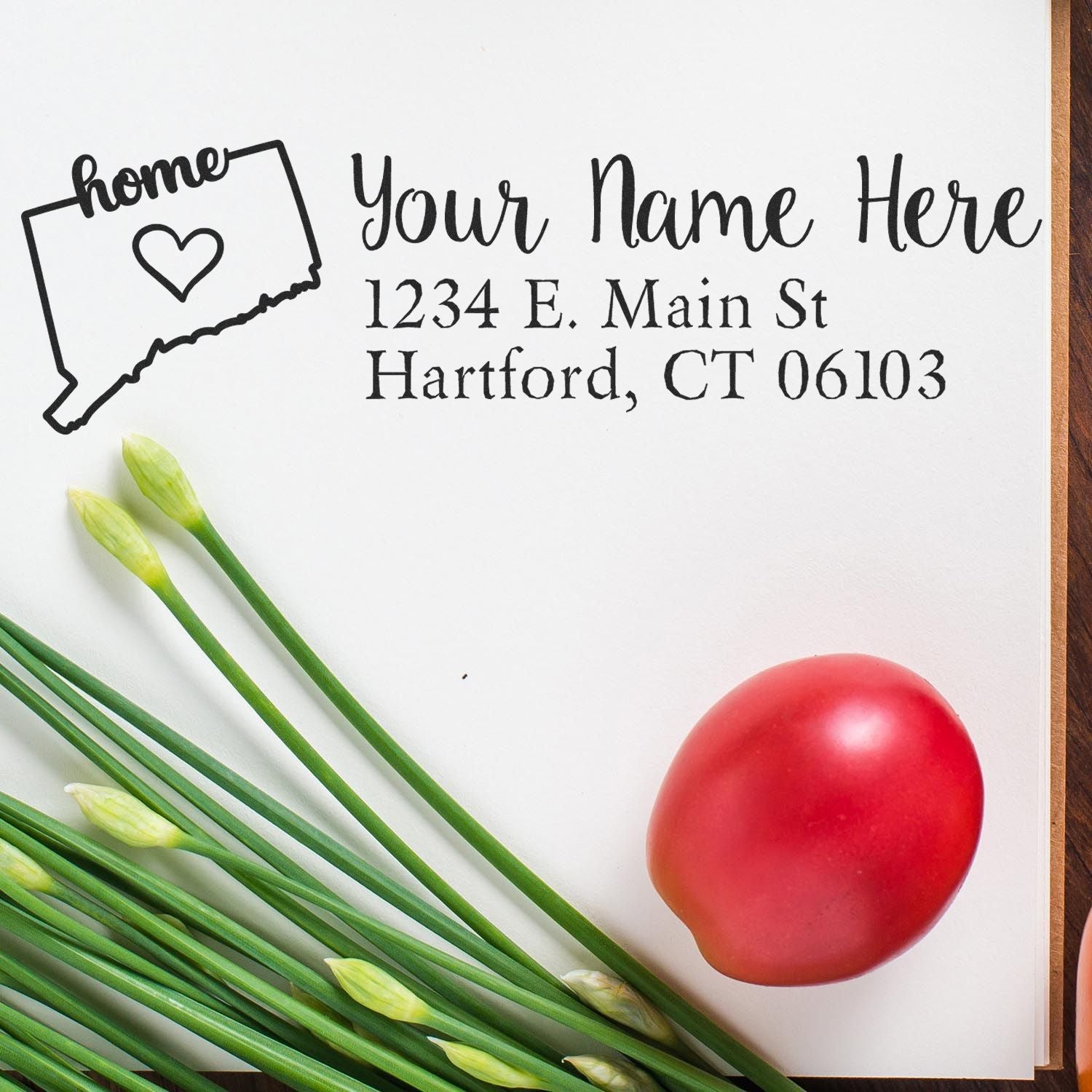 Connecticut Self-Inking State Love Address Stamp on paper with 'Your Name Here' and address, next to green onions and a red tomato, showcasing personalized design.