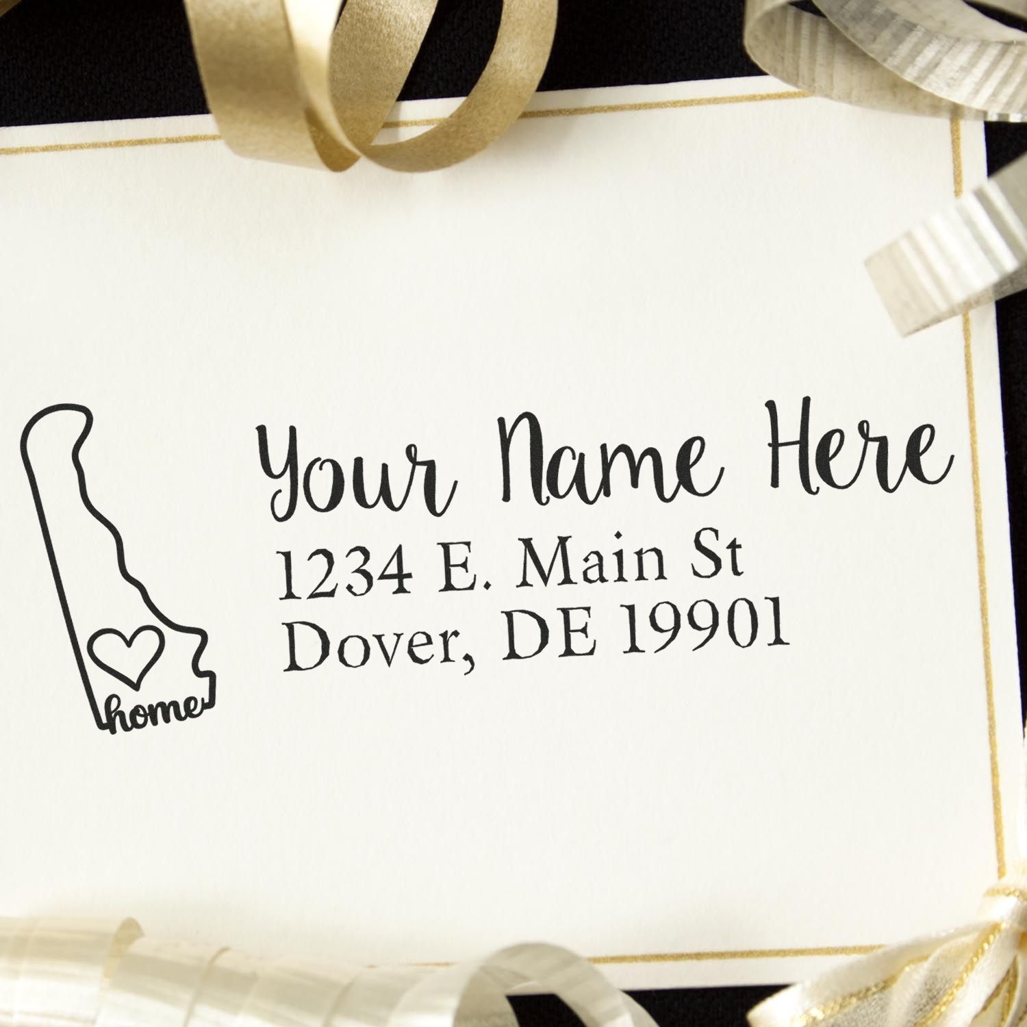 Delaware Self-Inking State Love Address Stamp on a card with Your Name Here, 1234 E. Main St, Dover, DE 19901 text, surrounded by gold and silver ribbons.