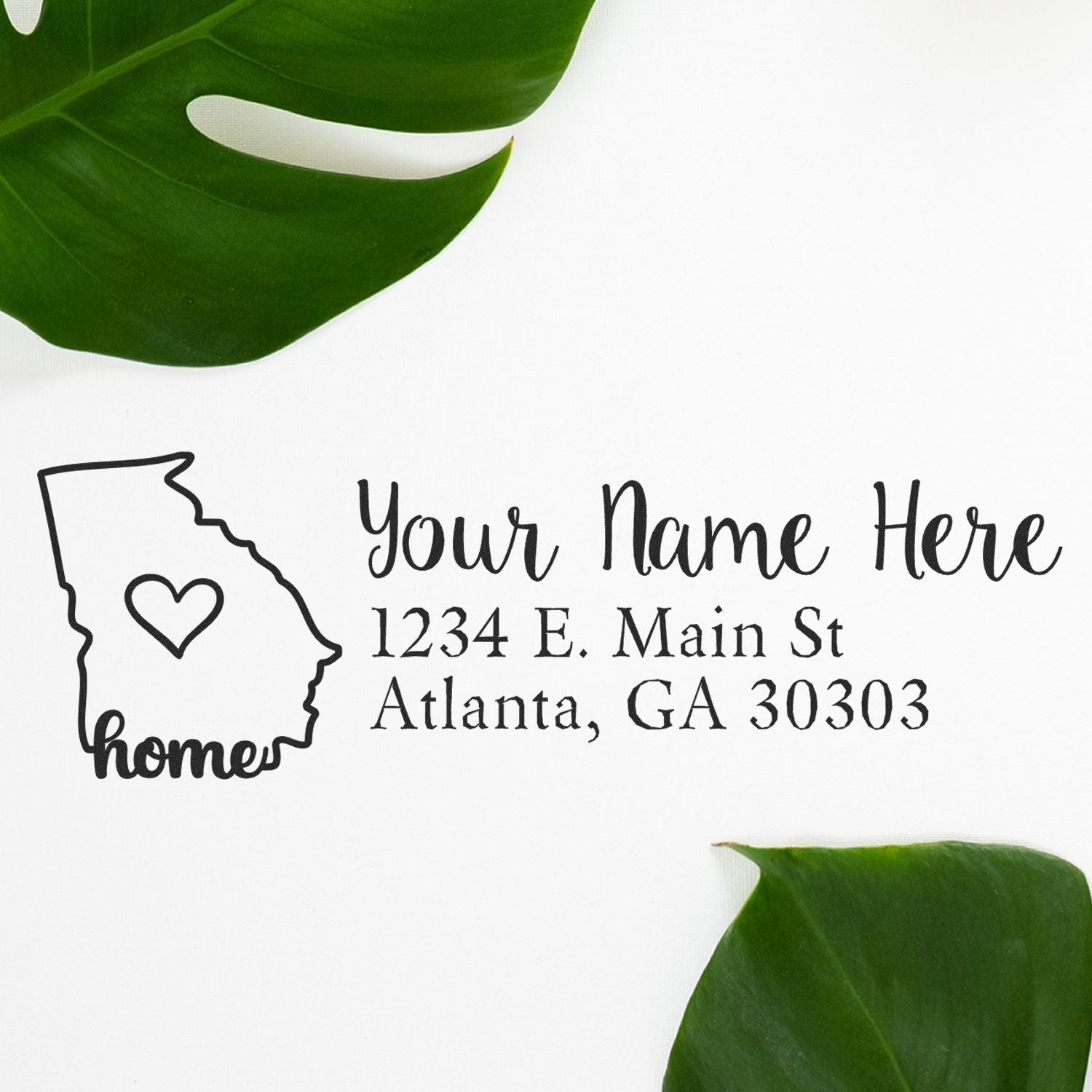 Slim Pre-Inked Georgia State Love Custom Address Stamp on white paper with a Georgia outline, heart, and sample address. Surrounded by green leaves for a stylish presentation.