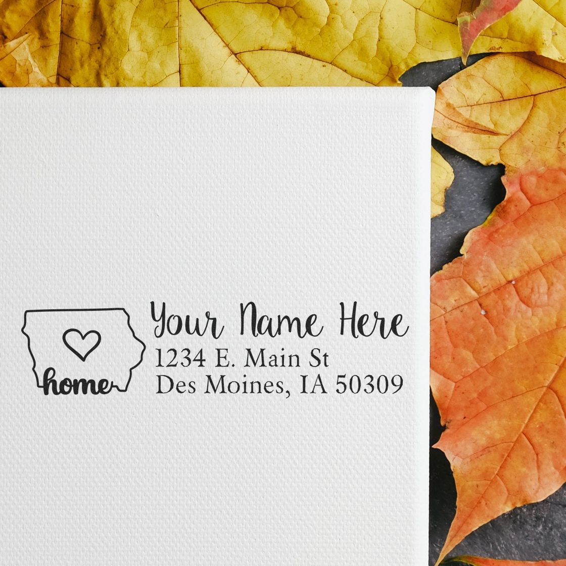 Iowa Self-Inking State Love Address Stamp on white paper with a heart in Iowa outline, surrounded by autumn leaves. Text: 'Your Name Here, 1234 E. Main St, Des Moines, IA 50309.'