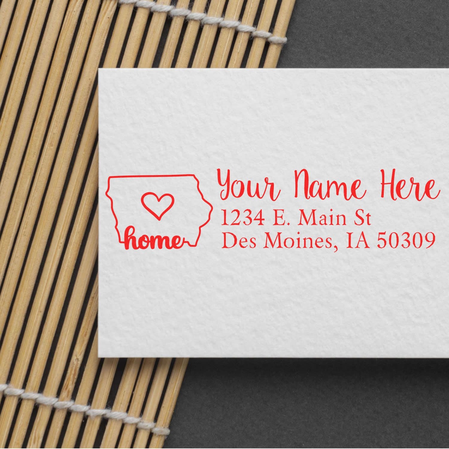 Iowa Self-Inking State Love Address Stamp on white card with red text, featuring a heart inside Iowa outline, placed on a bamboo mat. Text: 'Your Name Here, 1234 E. Main St, Des Moines, IA 50309'.