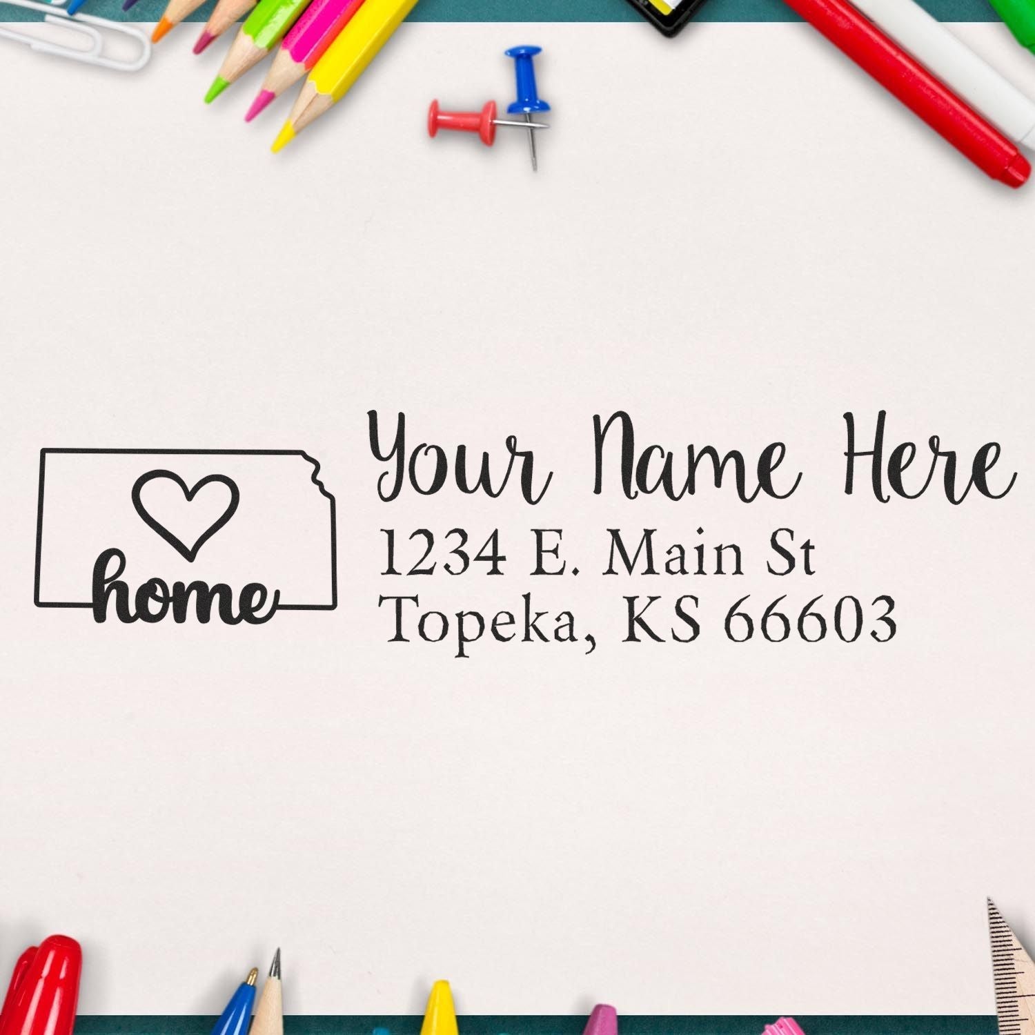 Wood Handle Kansas Custom Address Rubber Stamp on paper with a heart design and sample address. Surrounded by colorful pencils and a pushpin, showcasing its use for personalized mail.