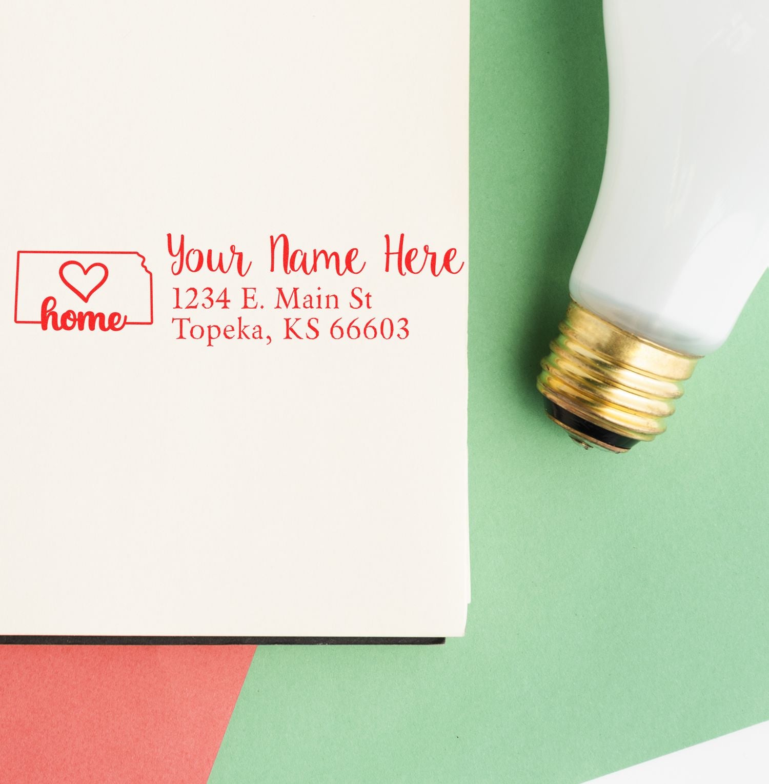 Wood Handle Kansas Custom Address Rubber Stamp on a white envelope with red ink, featuring a heart and home design, next to a light bulb on a colorful background.