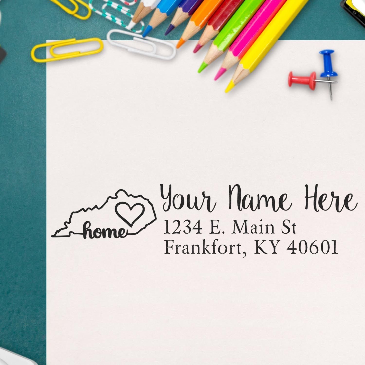 PSI Pre-Inked Personalized Kentucky State Love Address Stamp on paper with colorful pencils, paperclips, and push pins in the background.